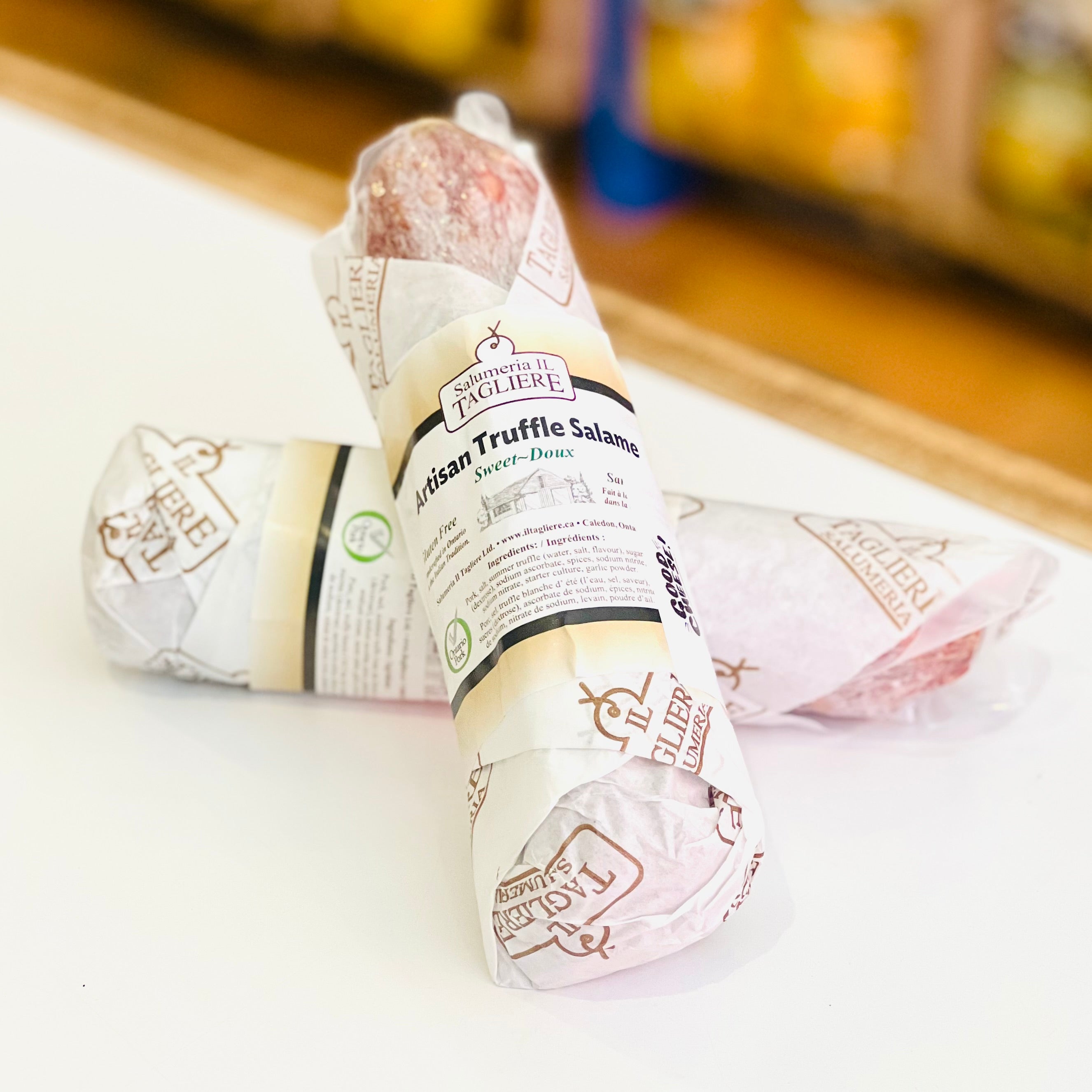 Two packages of truffle salami on a white surface with a blurred background.