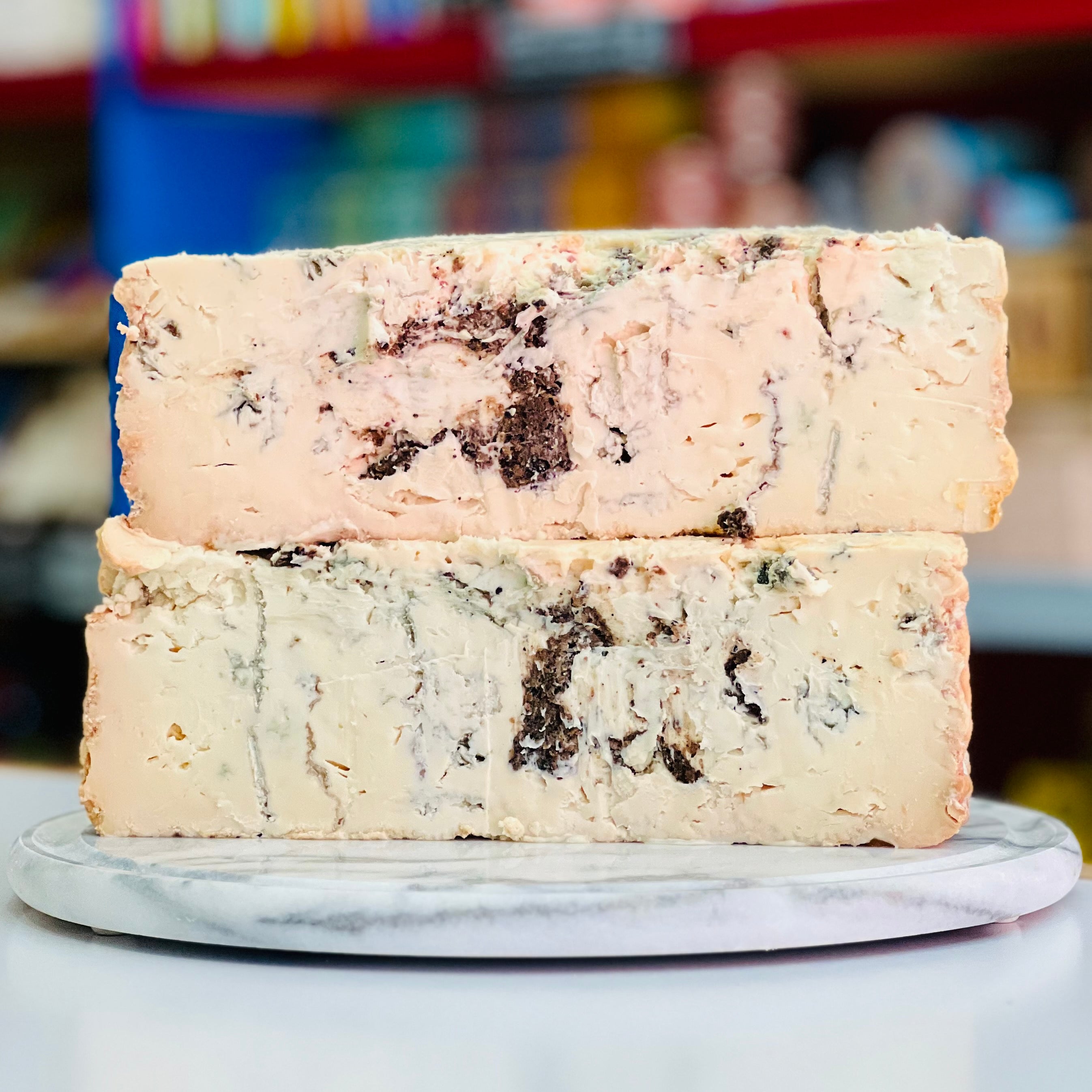Two blocks of cheese with visible herbs on a marble surface, blurred background