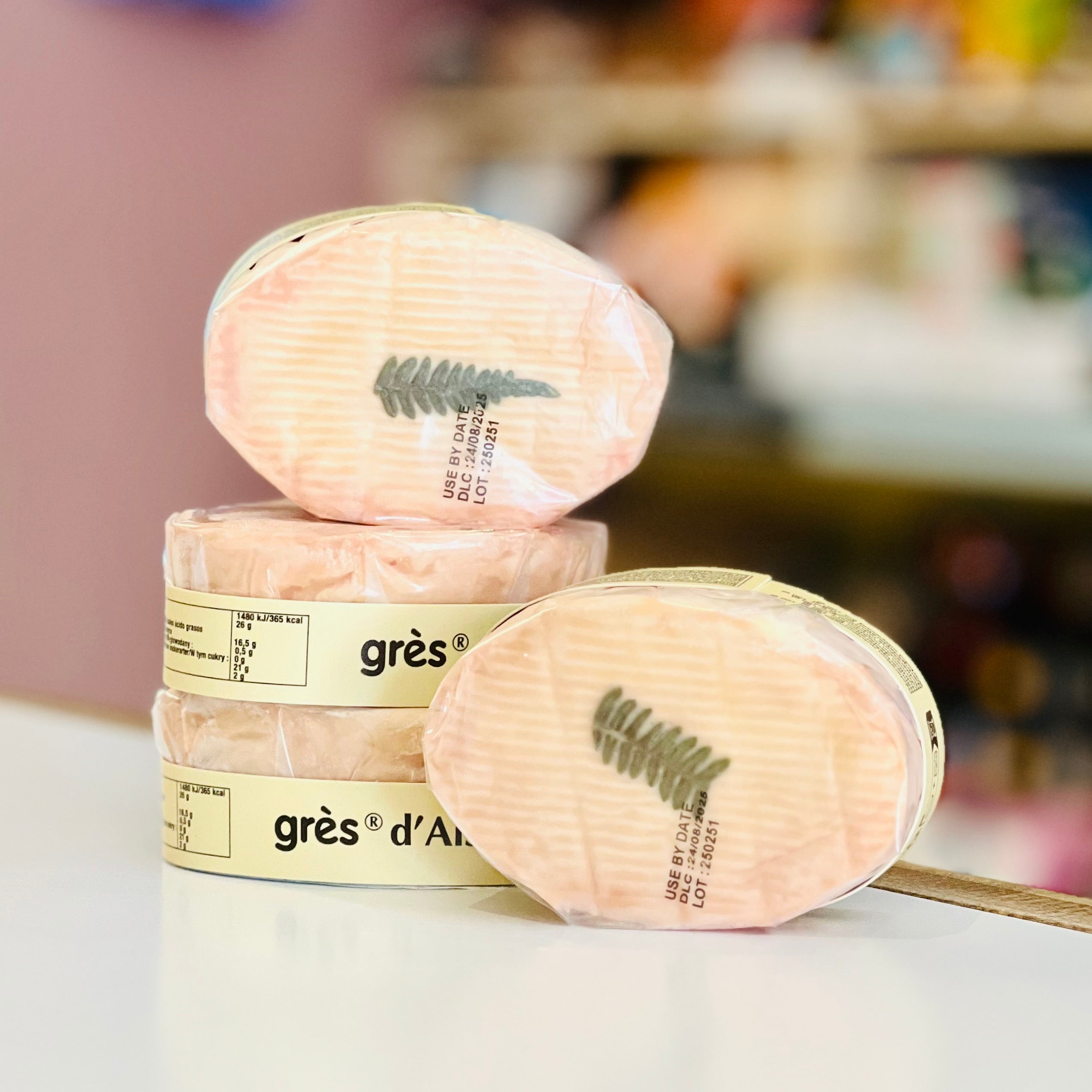 Four small oval wheels of cheese witha pink rind on a white surface with a blurred background.