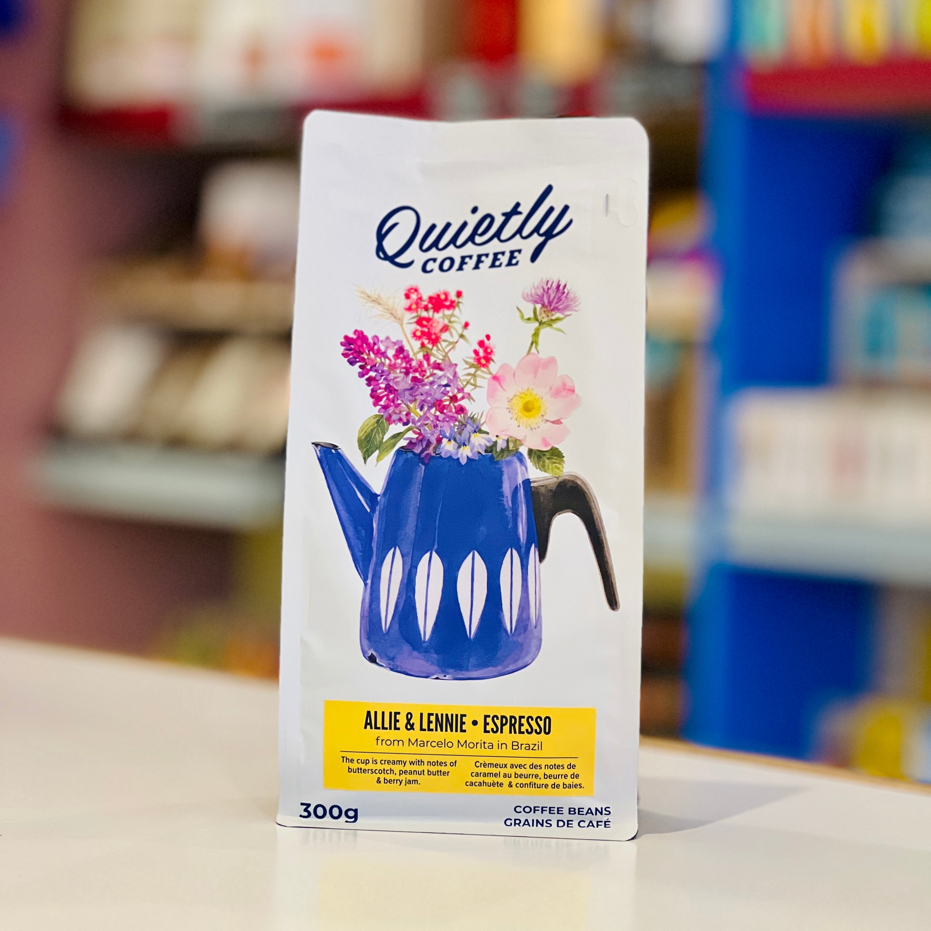 A package of 'Quietly Coffee' branded whole coffee beans with a floral design and a blue coffee pot illustration. The package is labeled 'Allie & Lennie Espresso' and indicates a weight of 300g.