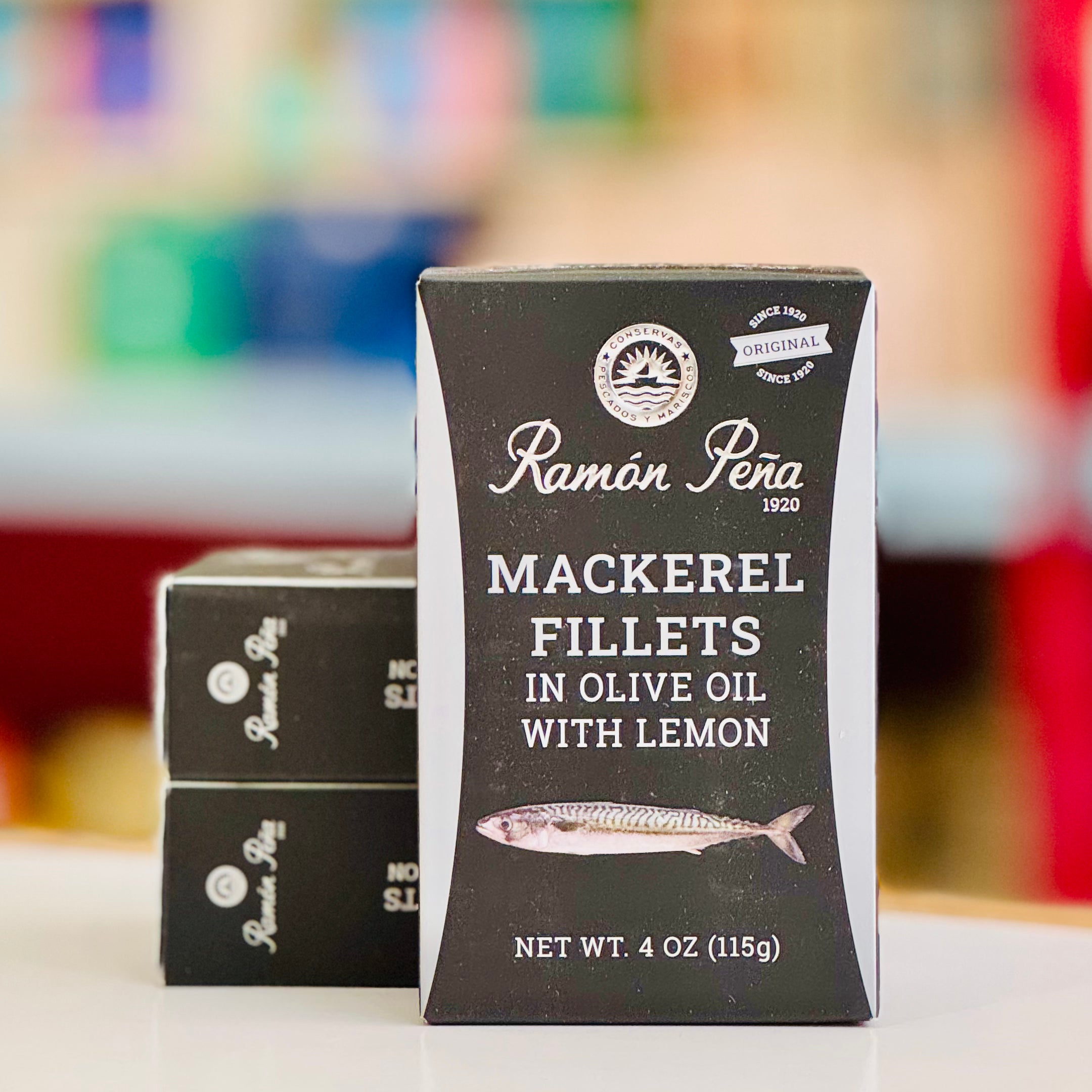 Packaging of Ramón Peña mackerel fillets in olive oil with lemon on a blurred background.