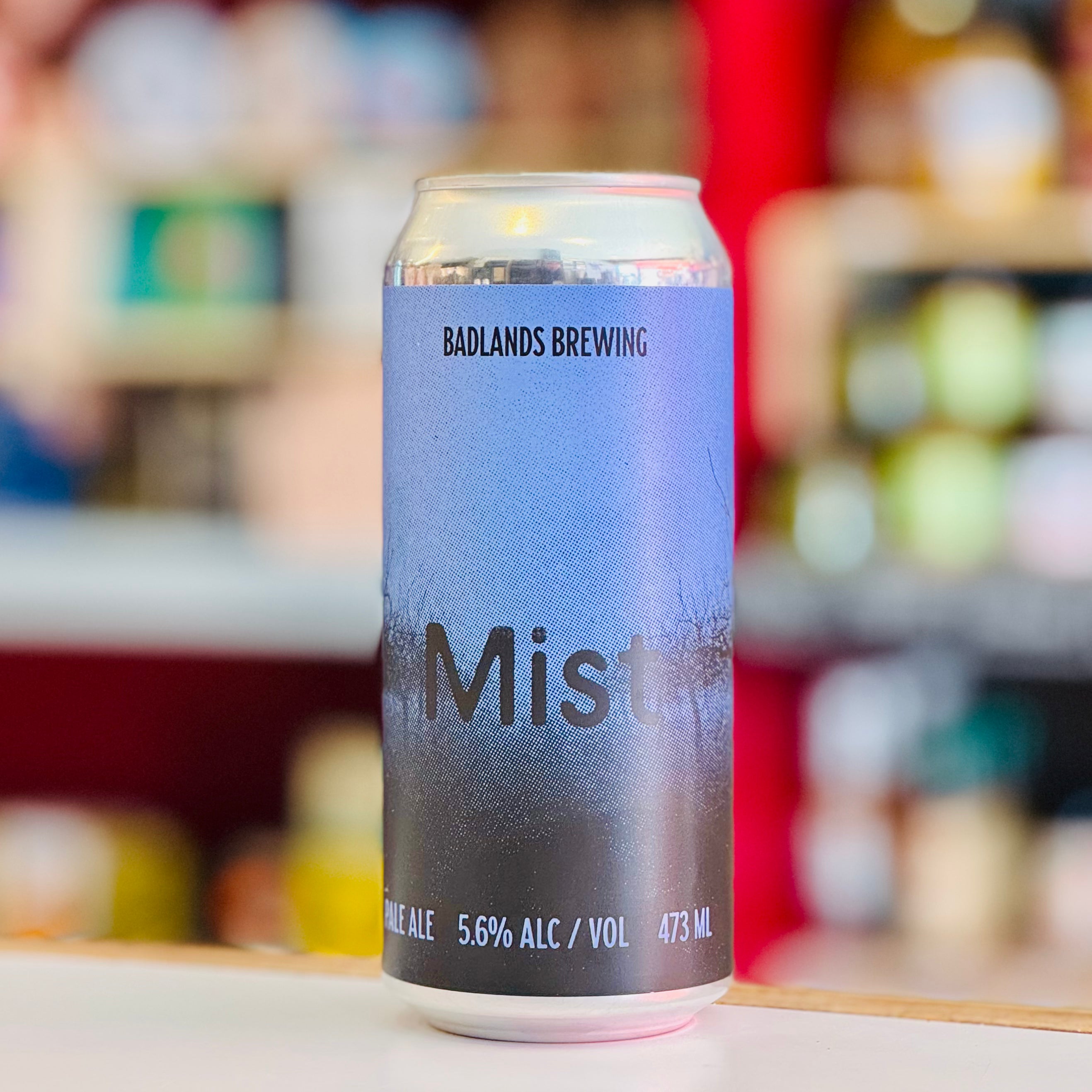 Beer can with 'Badlands Brewing' branding on a blurred store shelf background