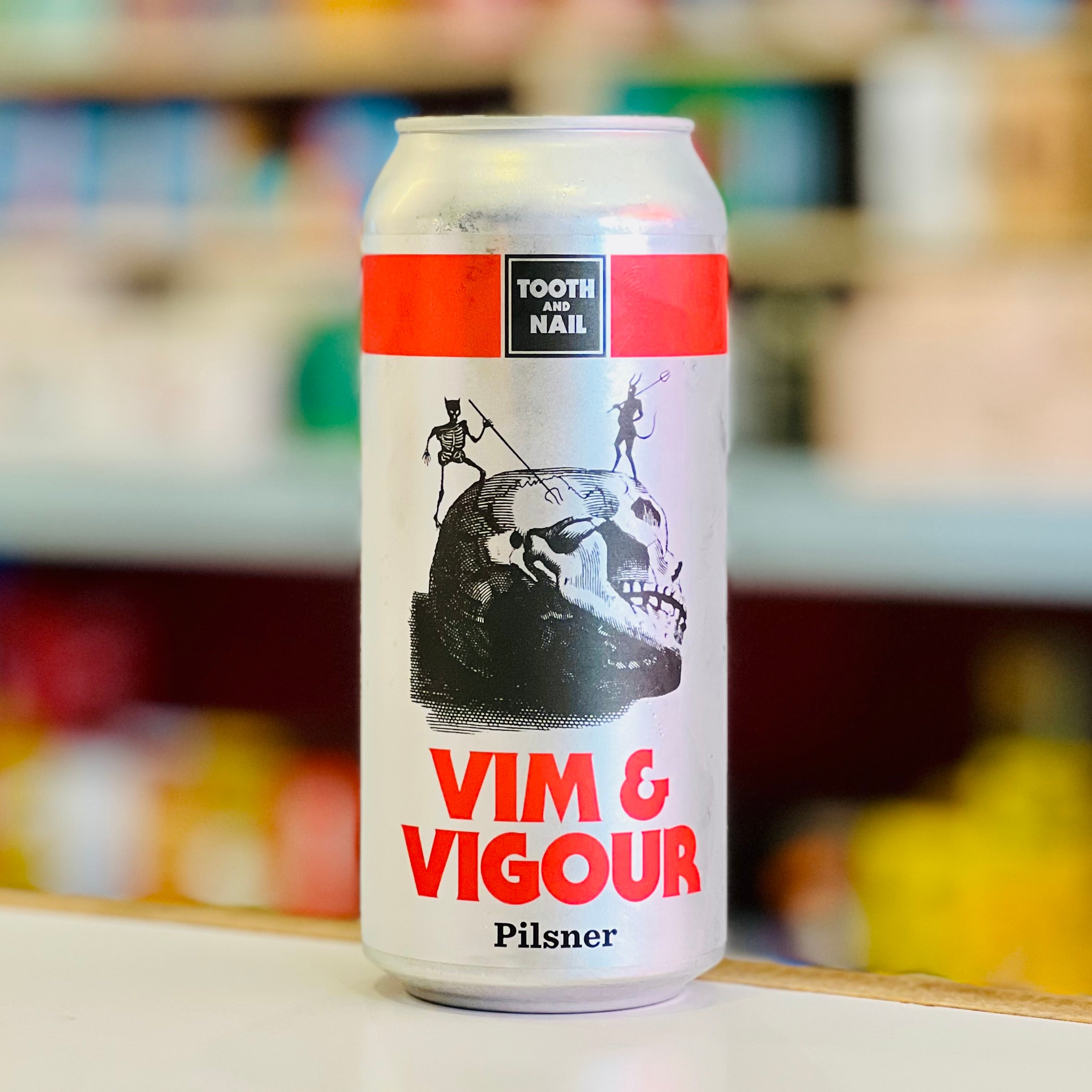 Can of Vim & Vigour Pilsner with 'Tooth and Nail' branding on a blurred store shelf background.