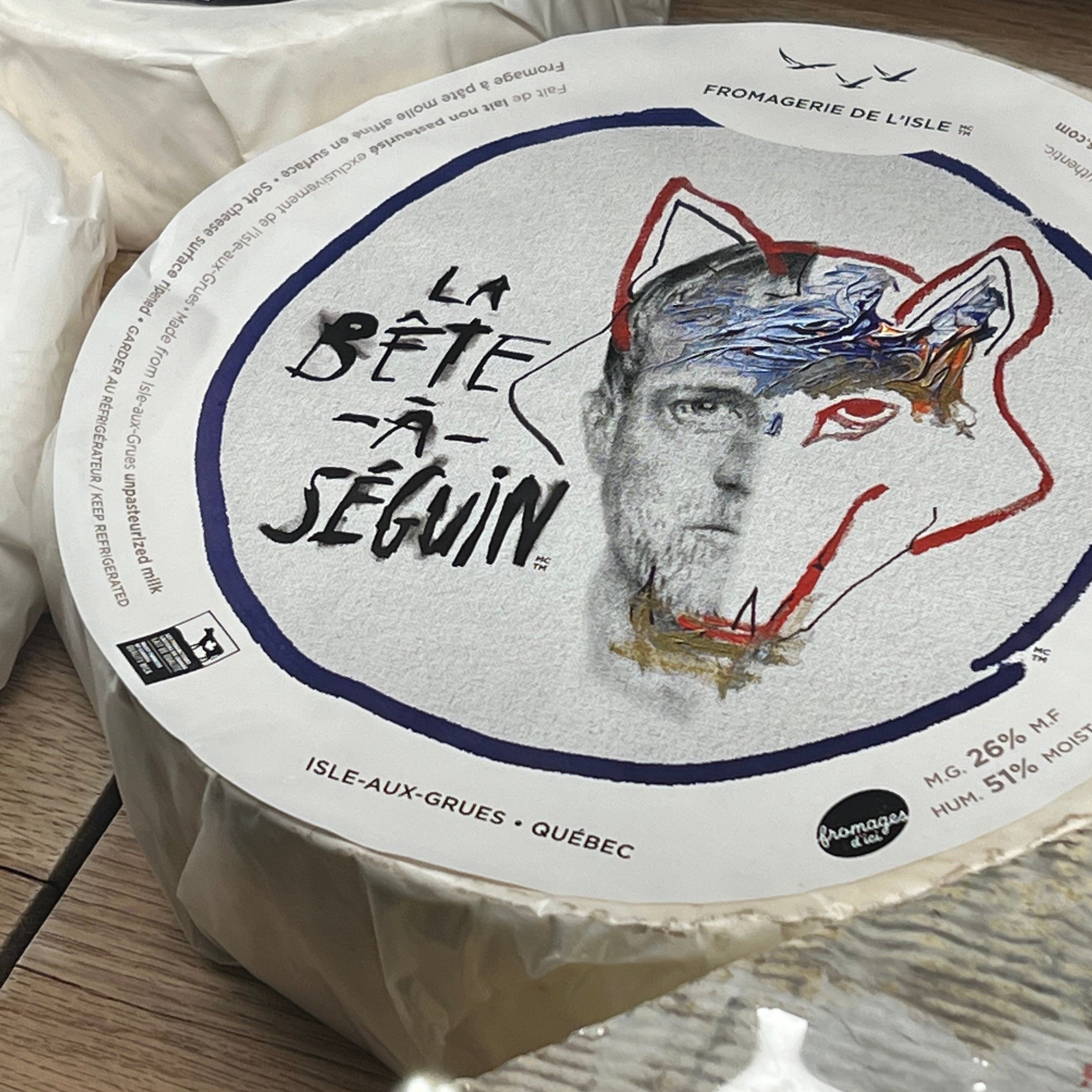 A round, wrapped wheel of bloomy rind cheese with an artistic drawing of a wolf's head overlayed by a man's face.