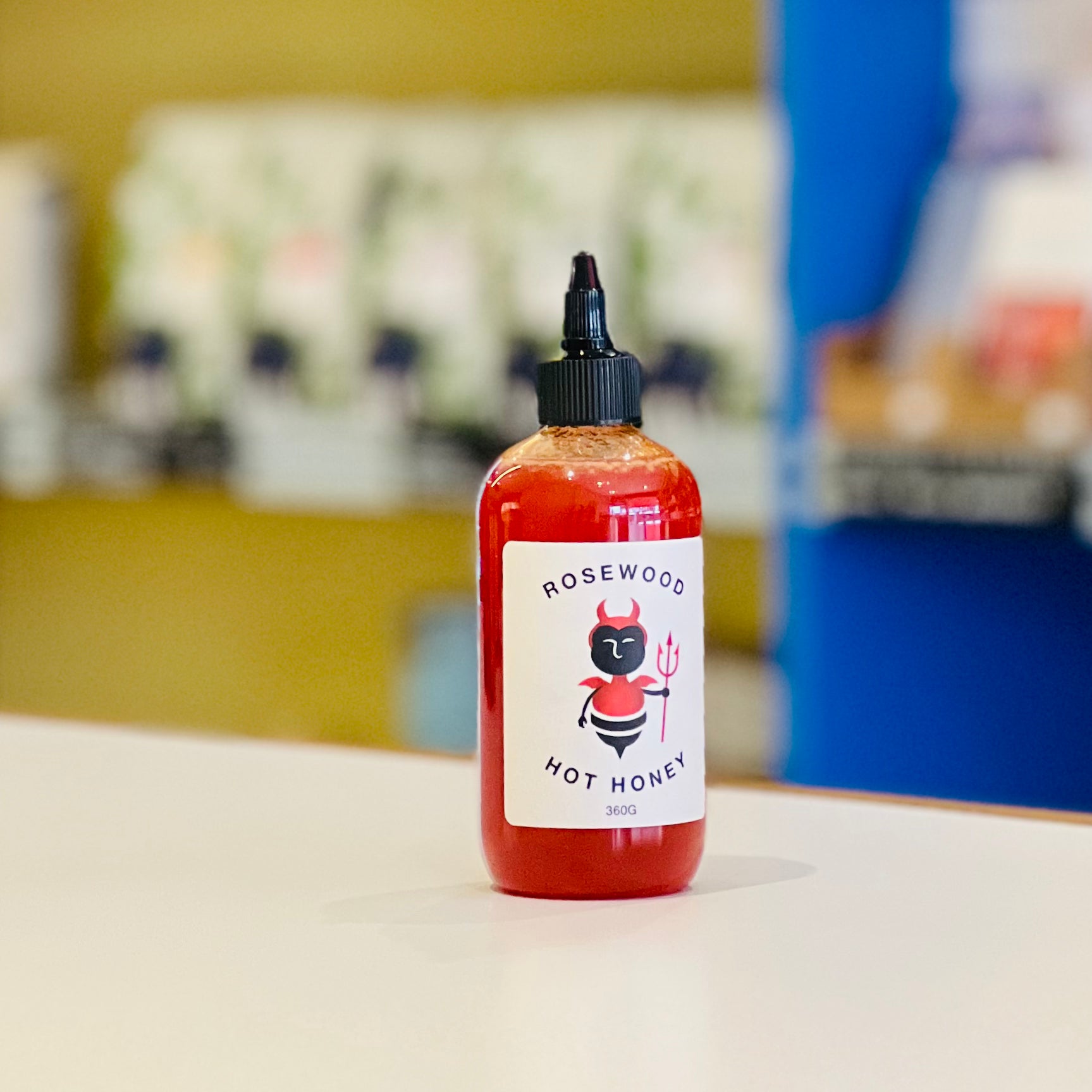 A bottle of Rosewood hot honey with a red label, placed on a counter.