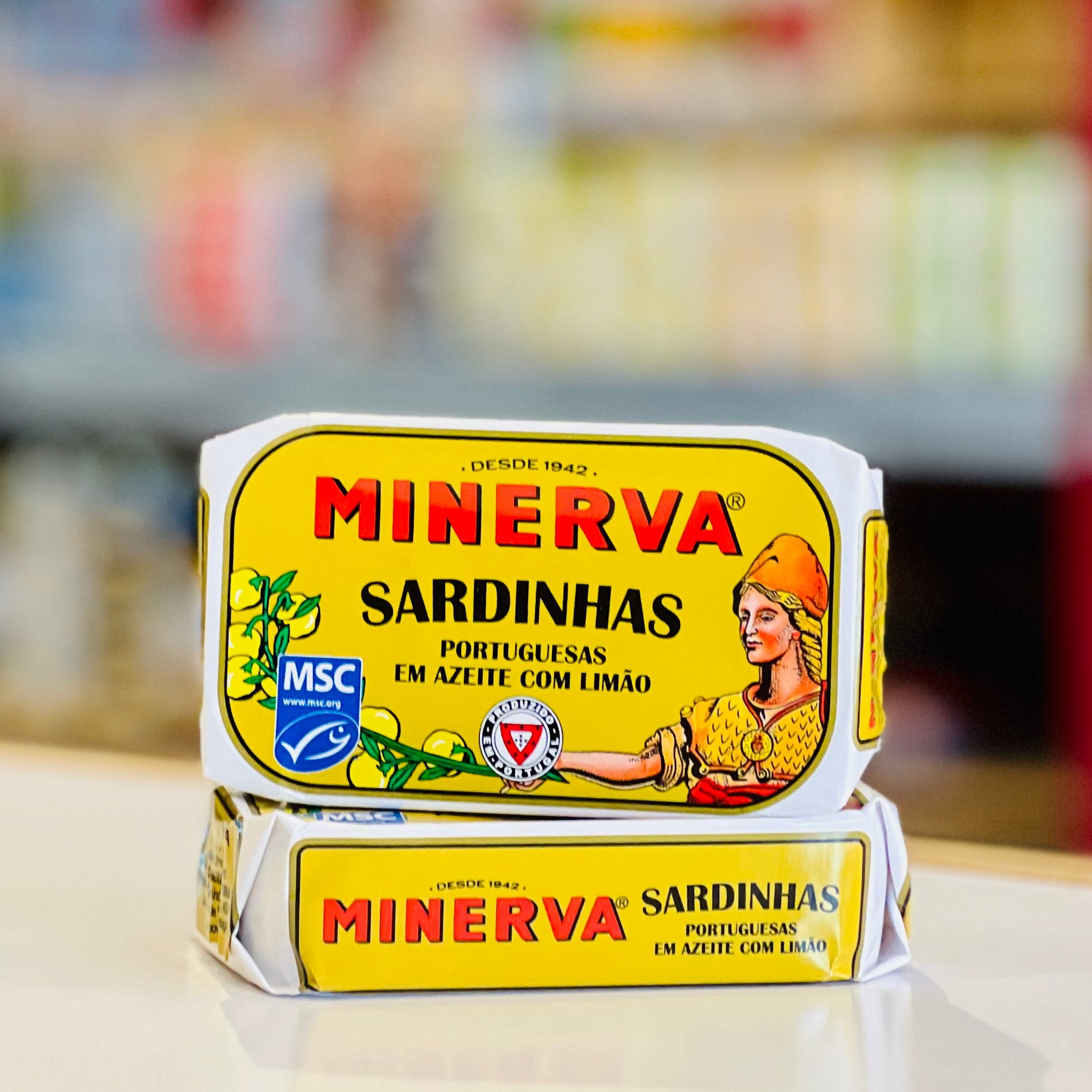 Two Minerva Sardinhas fish paste tubes stacked on a light surface with a blurred supermarket background.