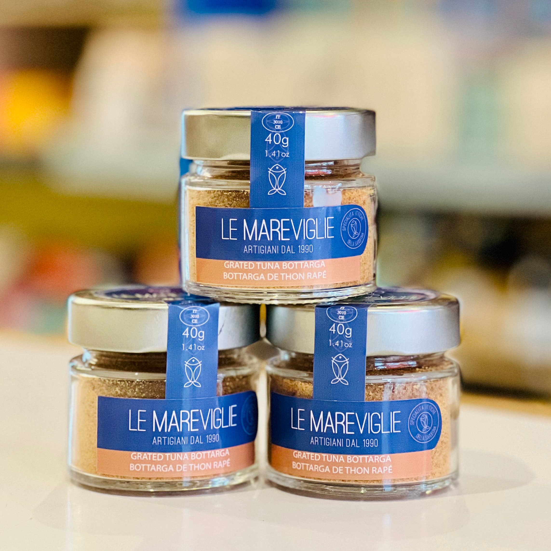 Three jars of 'Le Mareviglie' bottarga on a blurred background