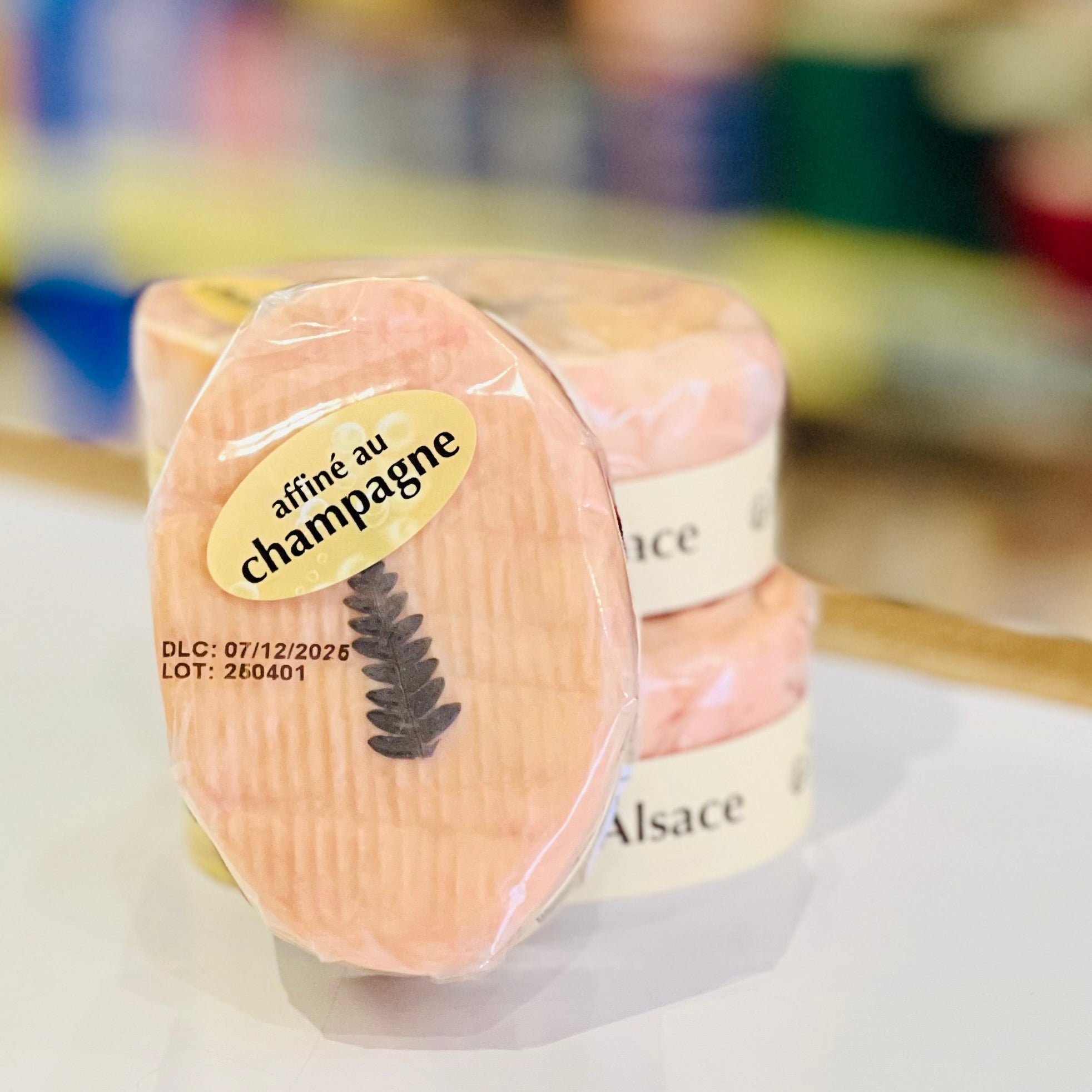 Soft, oval cheese with a peachy rind and 'affine au champagne' label on a blurred background