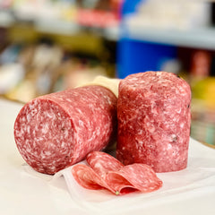 Two whole salamis and a sliced piece on a white surface with a blurred background