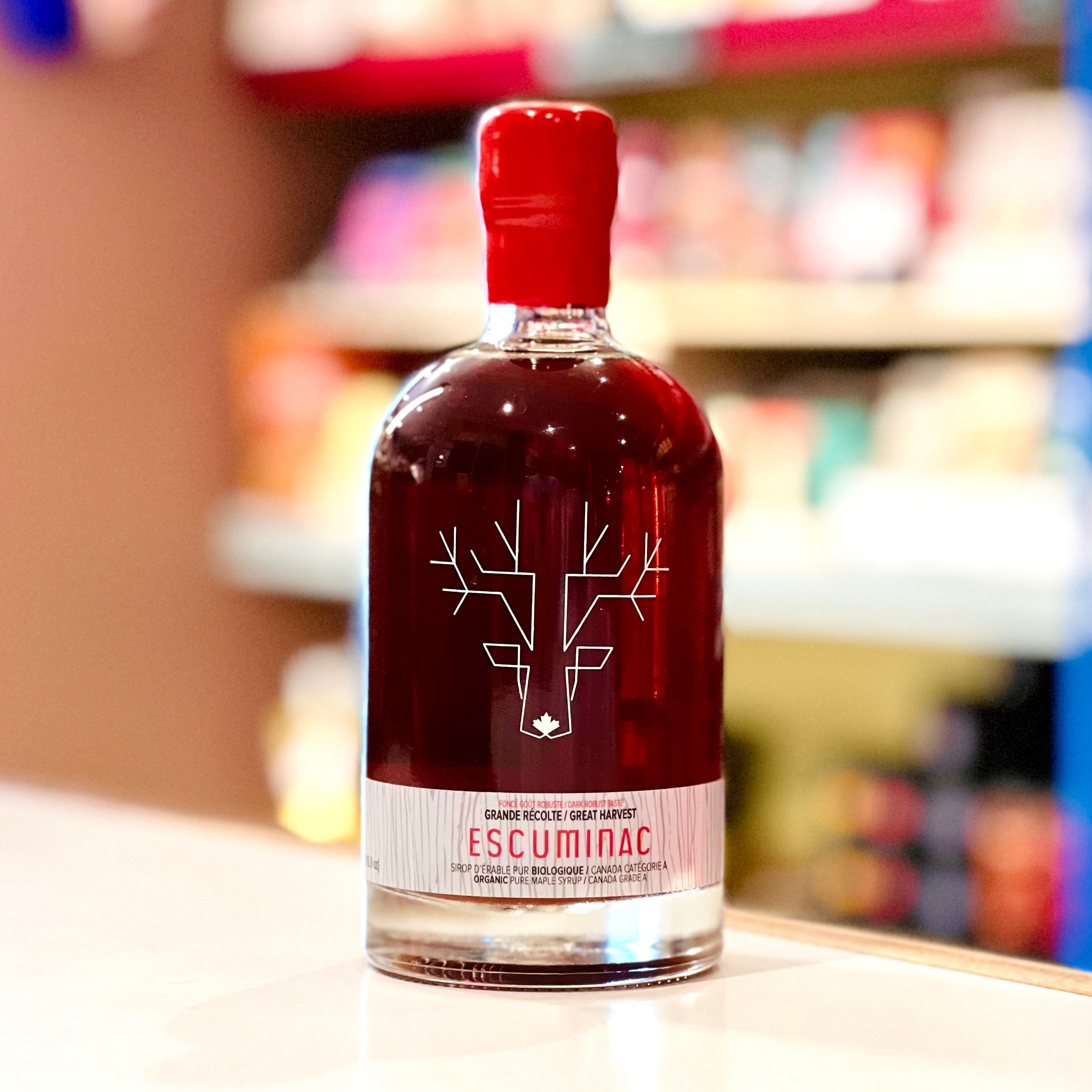 Bottle of Escuminac maple syrup with a red cap on a shelf.