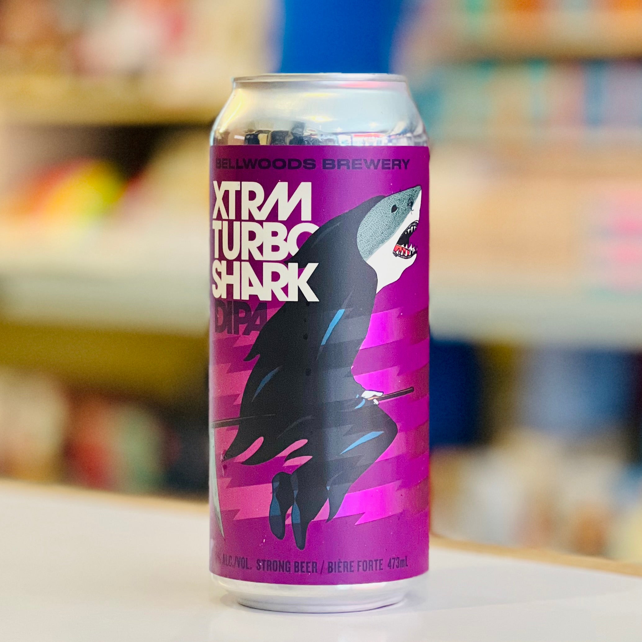 Beer can labeled 'Xtram Turbo Shark' from Hollywoods Brewery on a blurred store shelf background.