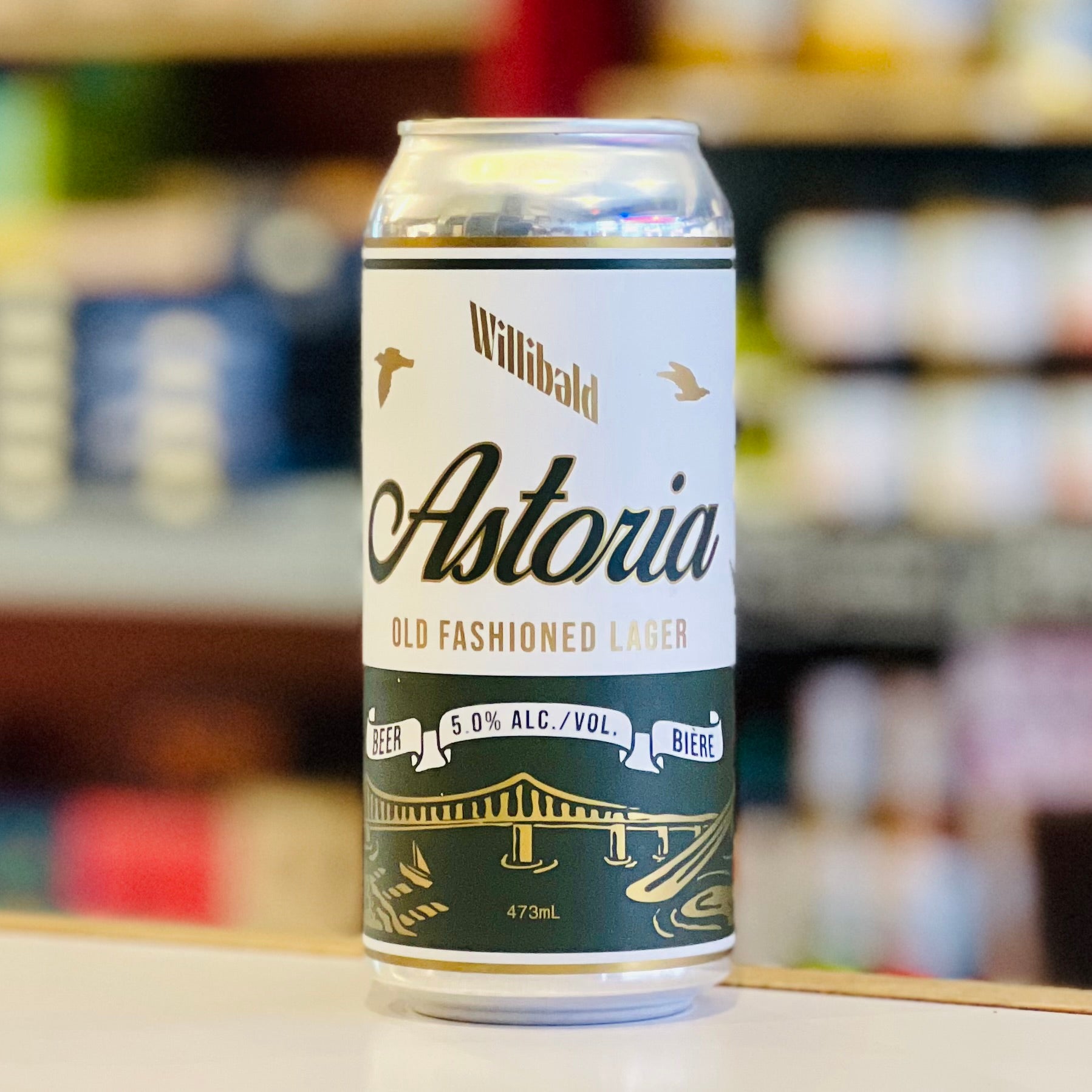 Can of Astoria Old Fashioned Lager with a blurred store shelf in the background
