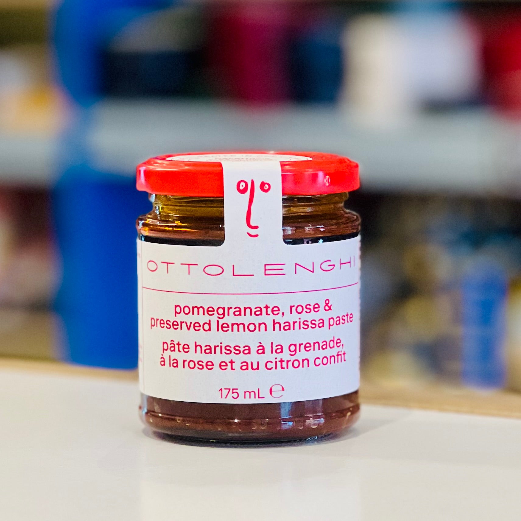 Jar of Ottolenghi pomegranate, rose & preserved lemon harissa paste with a red lid on a blurred background.