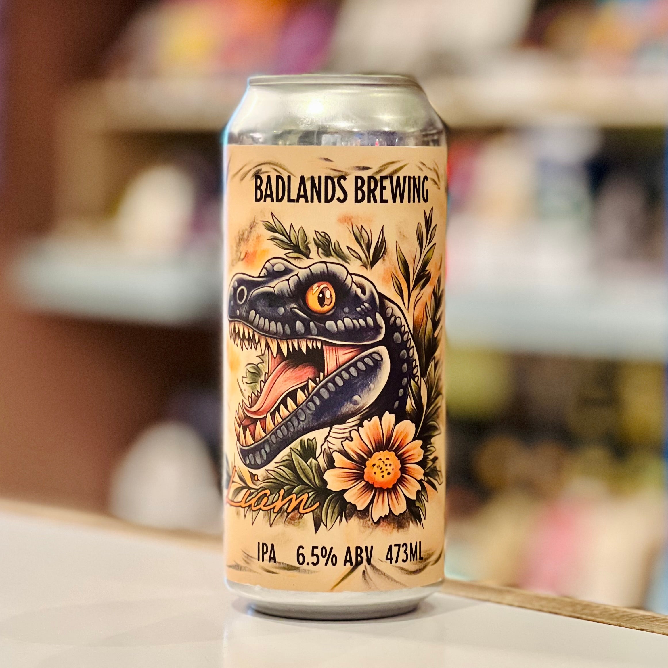 Beer can with Badlands Brewing logo and dinosaur design on a blurred background