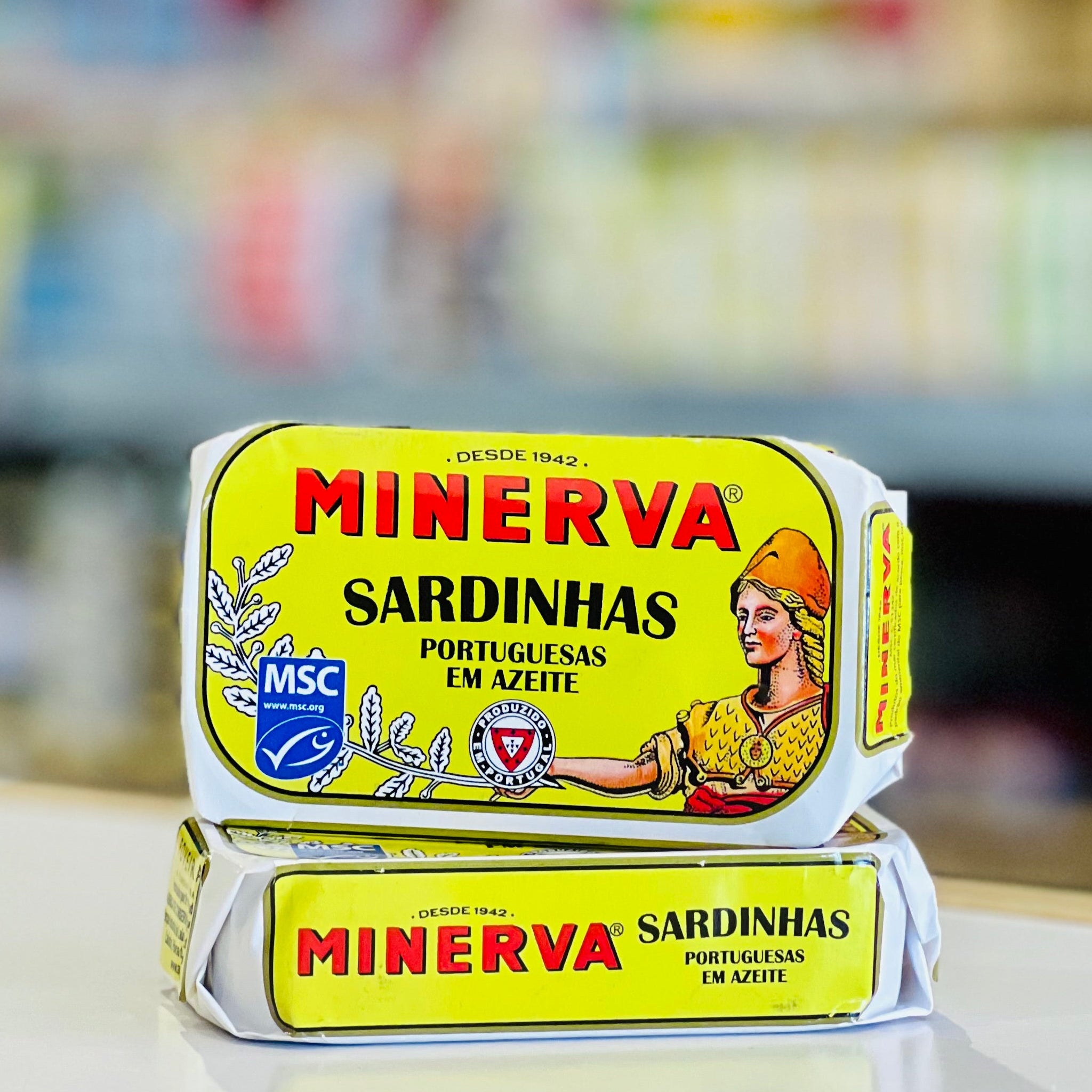 Two packages of Minerva Sardinhas (Portuguese canned salmon) stacked on a white counter with a blurred shop background.