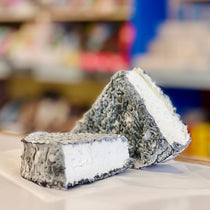 Two wedges of ashed goat cheese on a white surface with a blurred background
