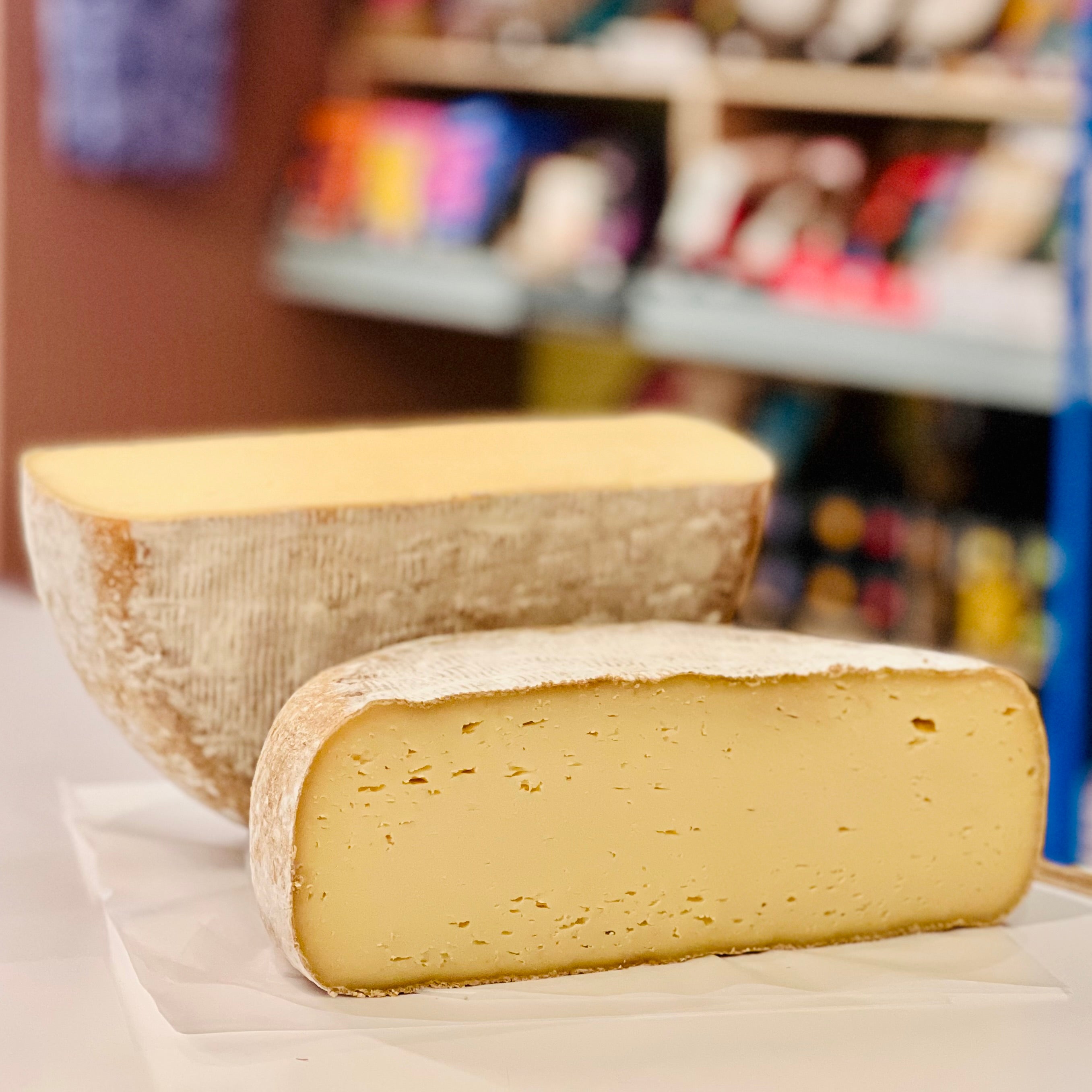 Two wedges of cheese on a white surface with a blurred store shelf in the background