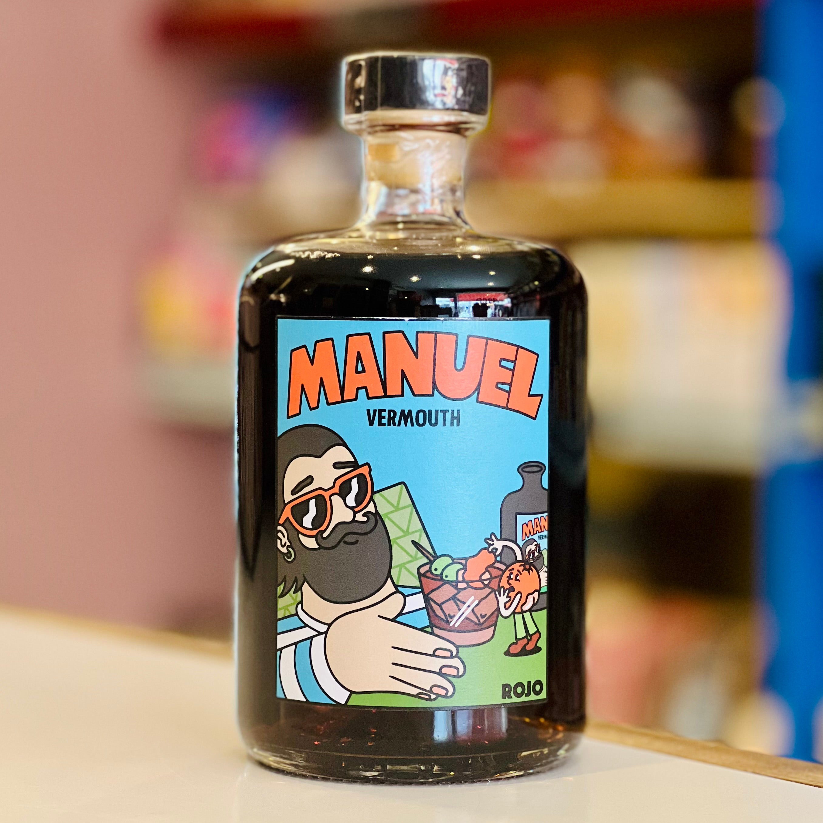 Bottle of Manuel Vermouth with a colorful label featuring a cartoon character on a blurred background.