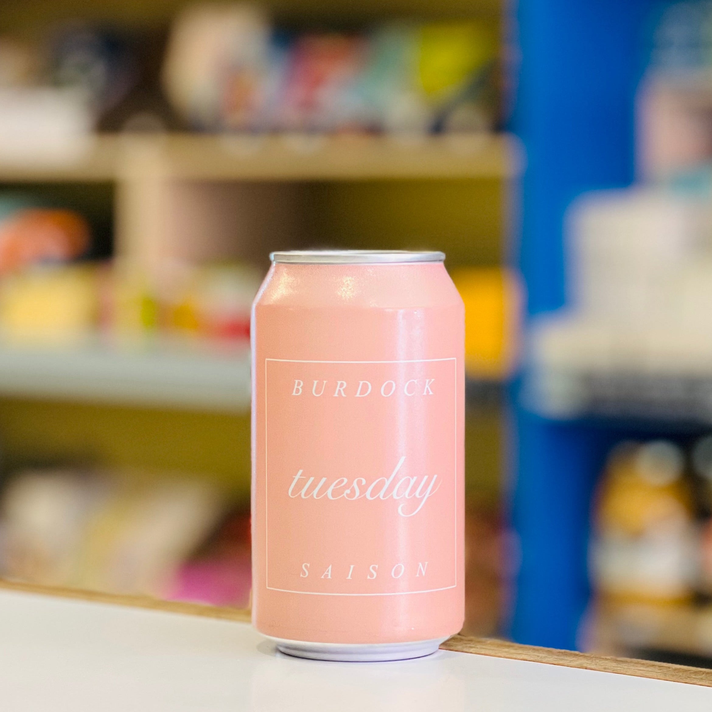 Pink can with 'Burdock Tuesday' text on a shelf in a store.