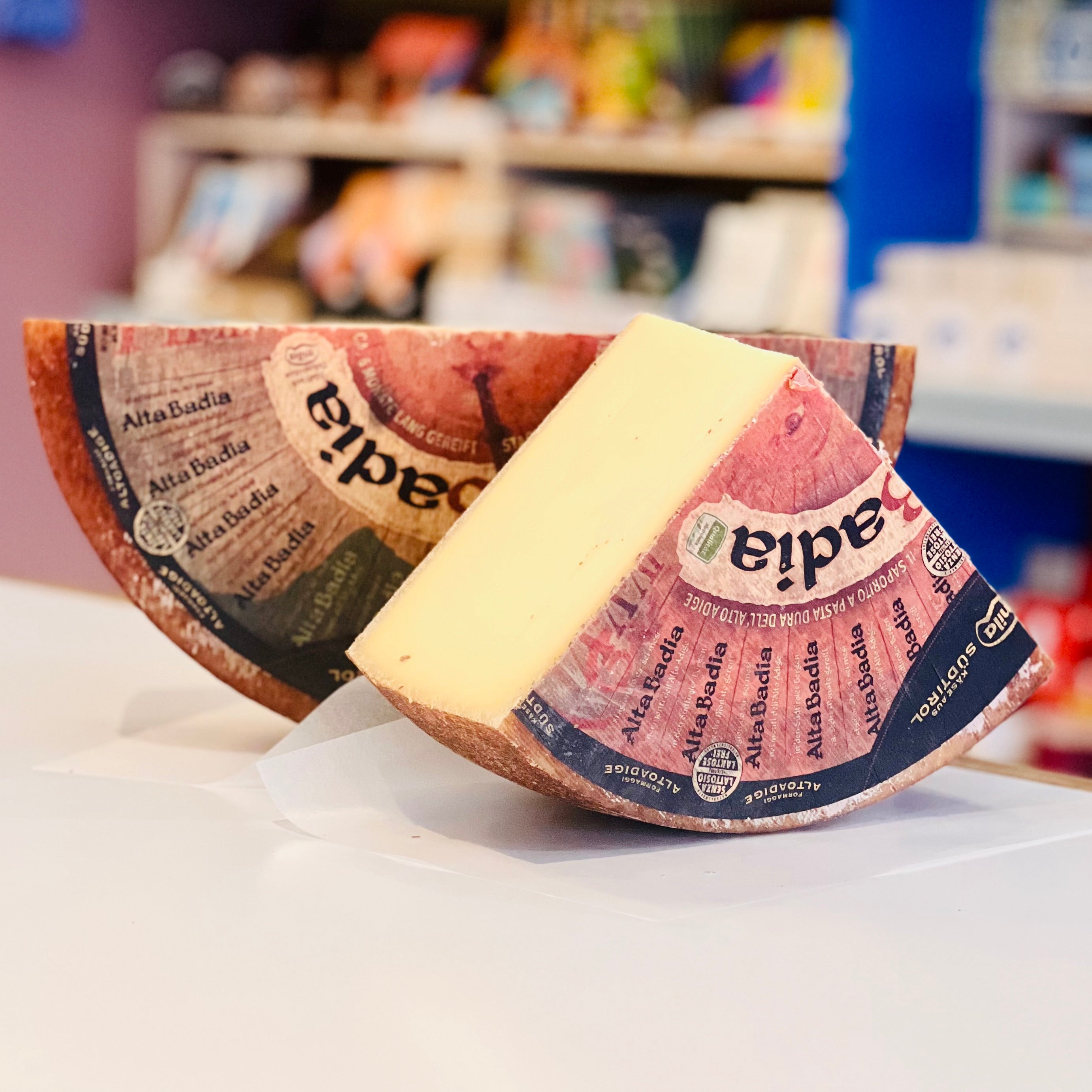 Two wedges of Alta-Badia cheese with packaging on a white surface.


