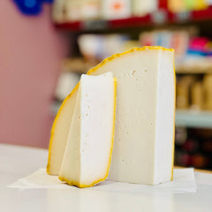 Block of white cheese with a yellow rind on a white surface, blurred background