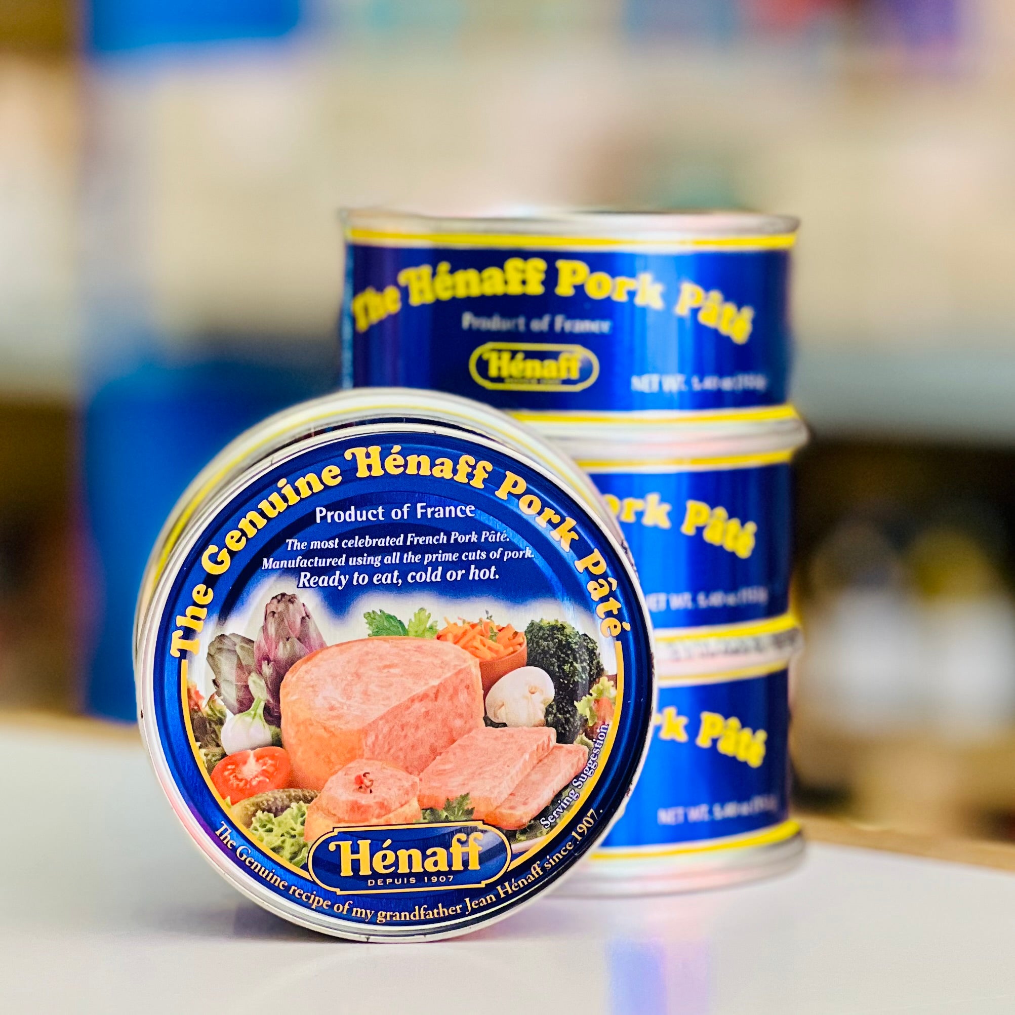Two cans of Hénaff pork páté on a table with a blurred background