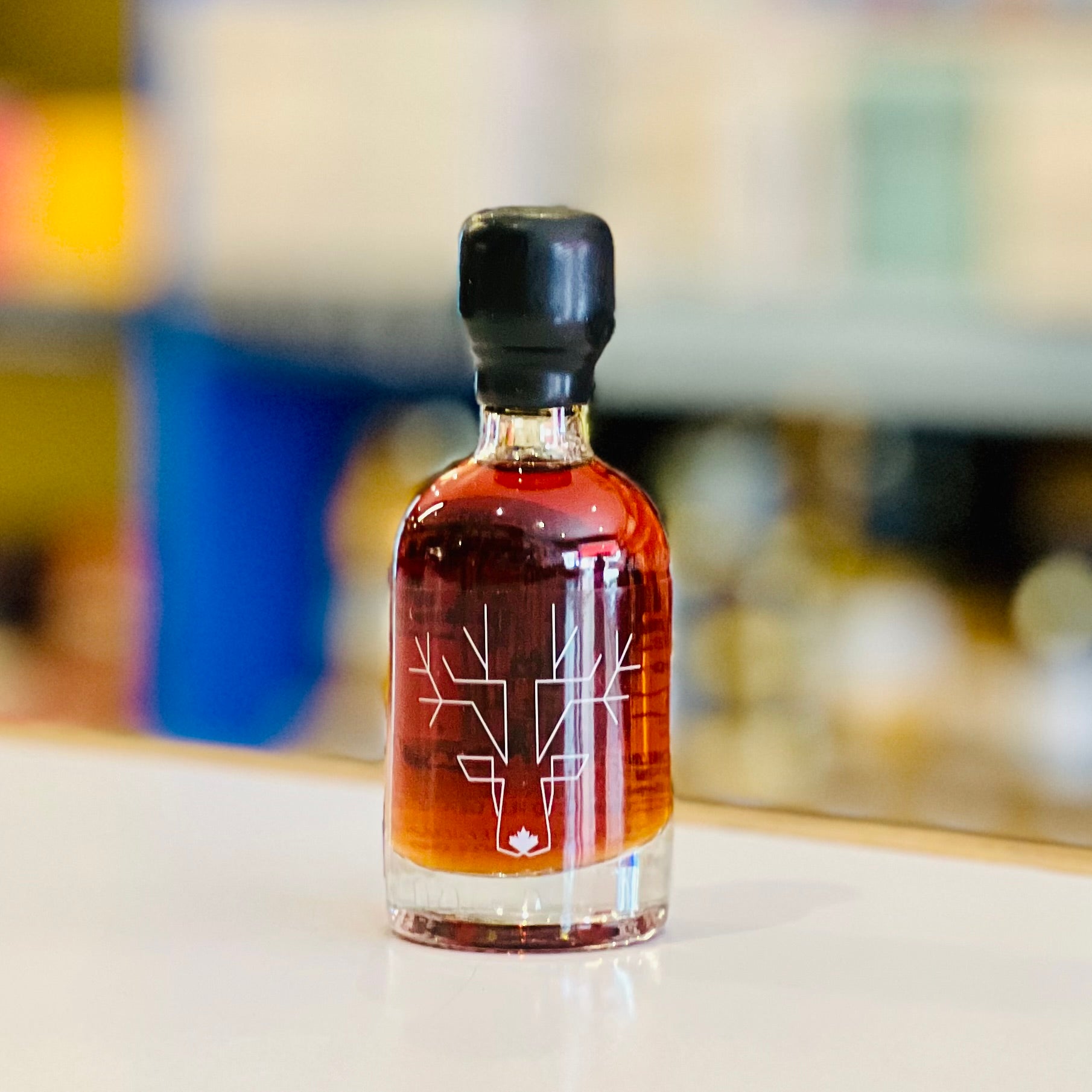 Small bottle of amber liquid with a black cap on a white surface, blurred background