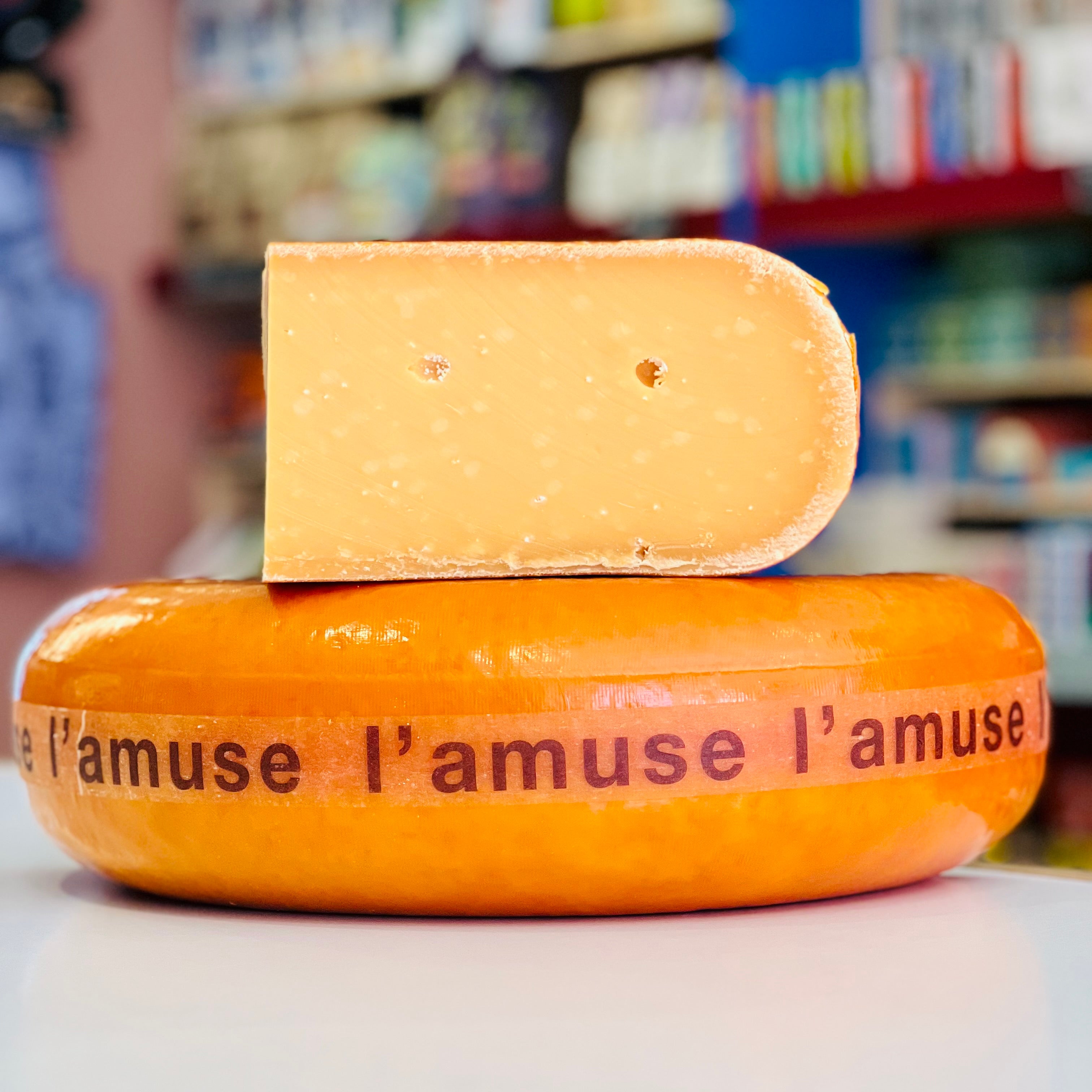 Cheese wheel with a piece cut off, labeled 'l'amuse', in a store setting.