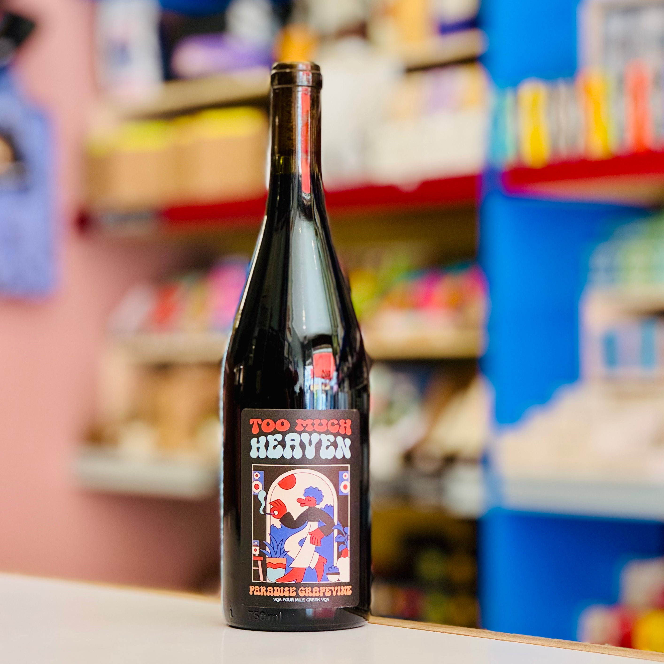 Bottle of 'Too Much Heaven' wine with a colorful label in a store setting