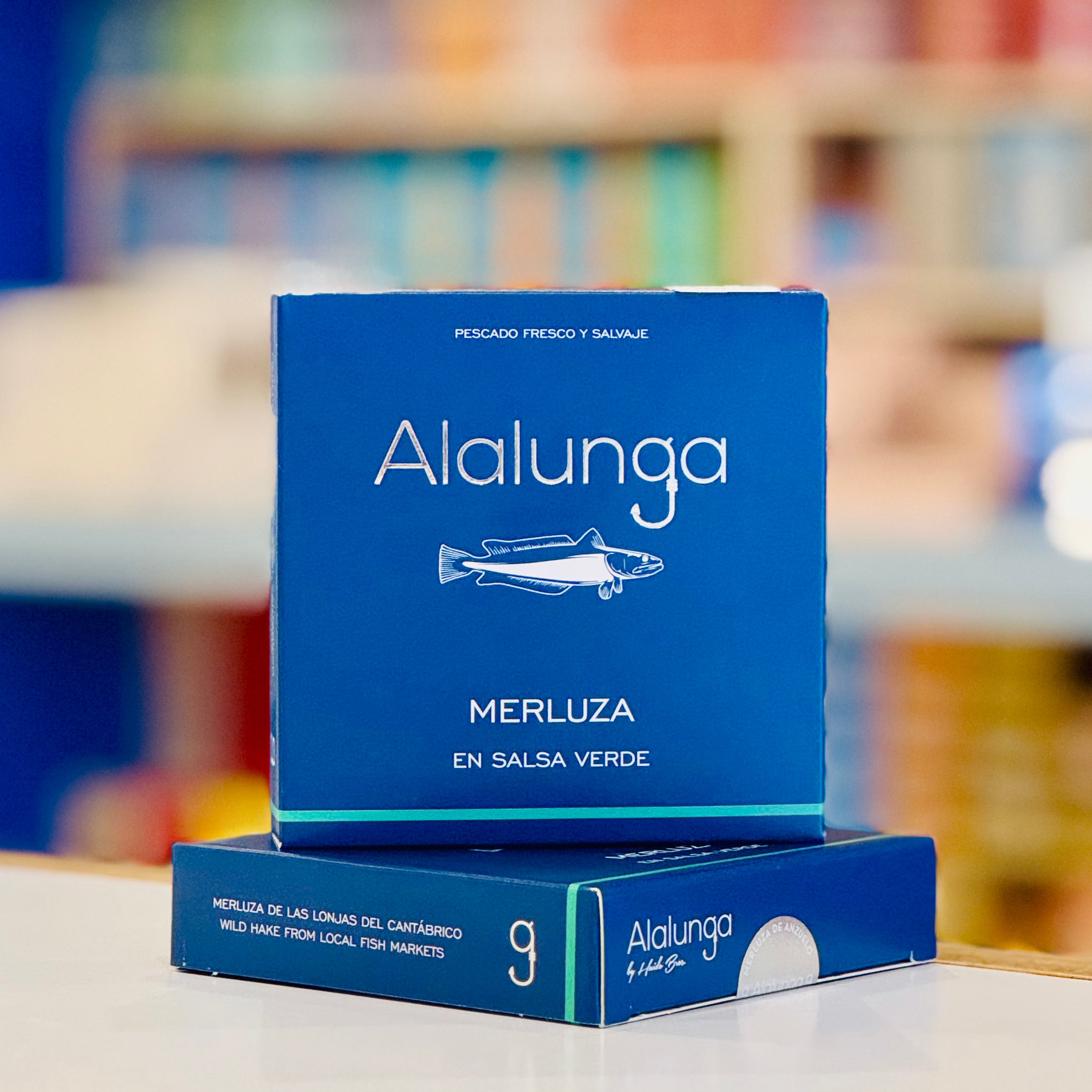 Blue 'Alalunga' product packaging on a blurred bookshelf background