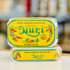 Two tins of 'Nuri' spiced sardines in olive oil on a blurred background
