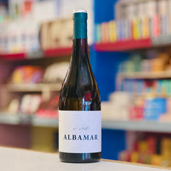 Wine bottle labeled 'Albamar' on a shelf with colorful products in the background