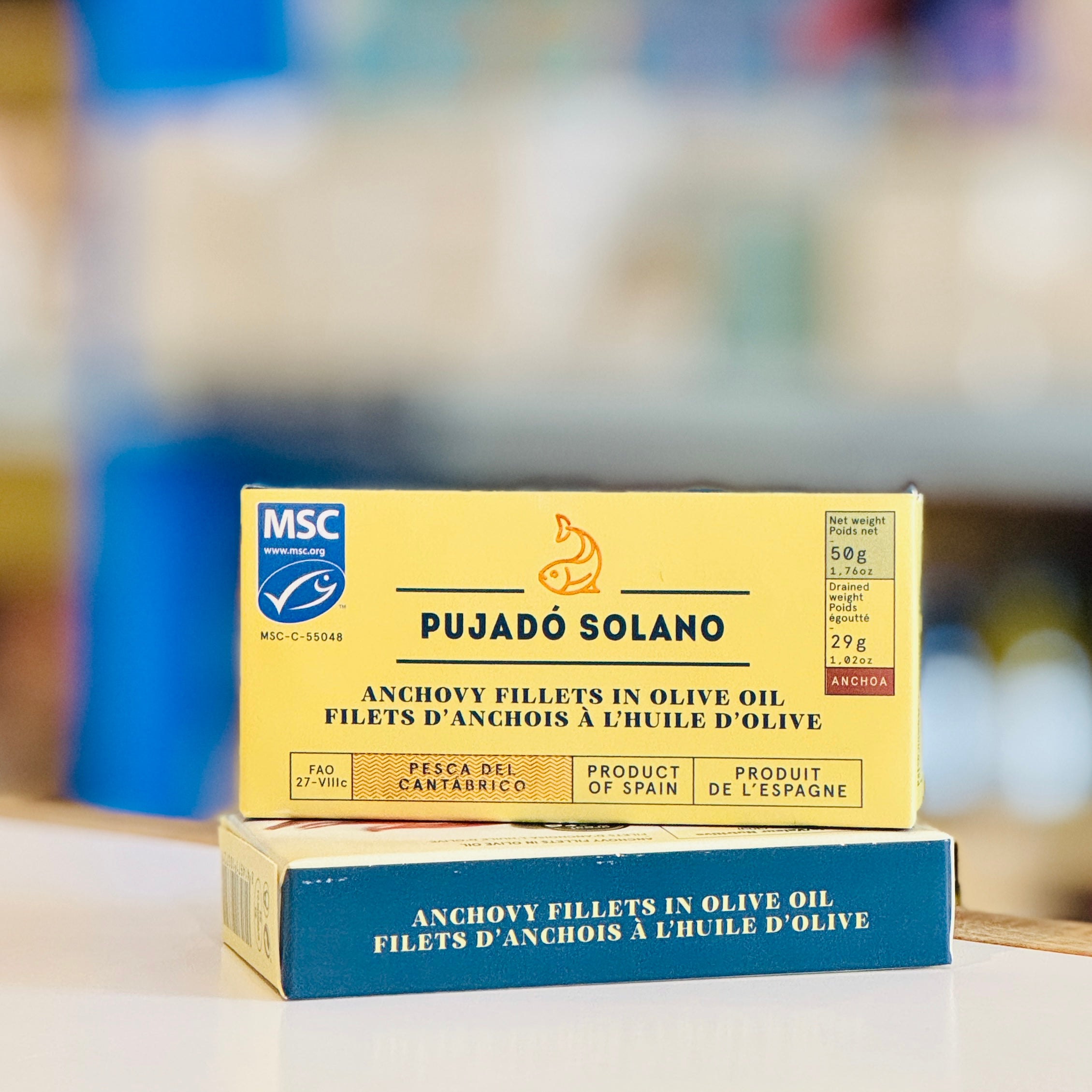 Two boxes of Pujado Solano anchovy fillets in olive oil on a blurred background