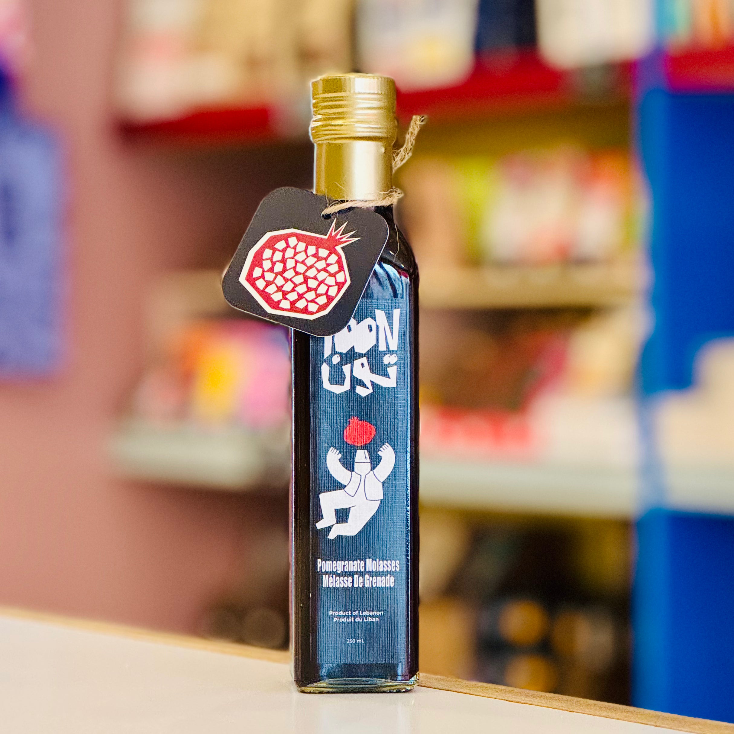 Bottle of Pomegranate Molasses with a gold cap and black label on a shelf.