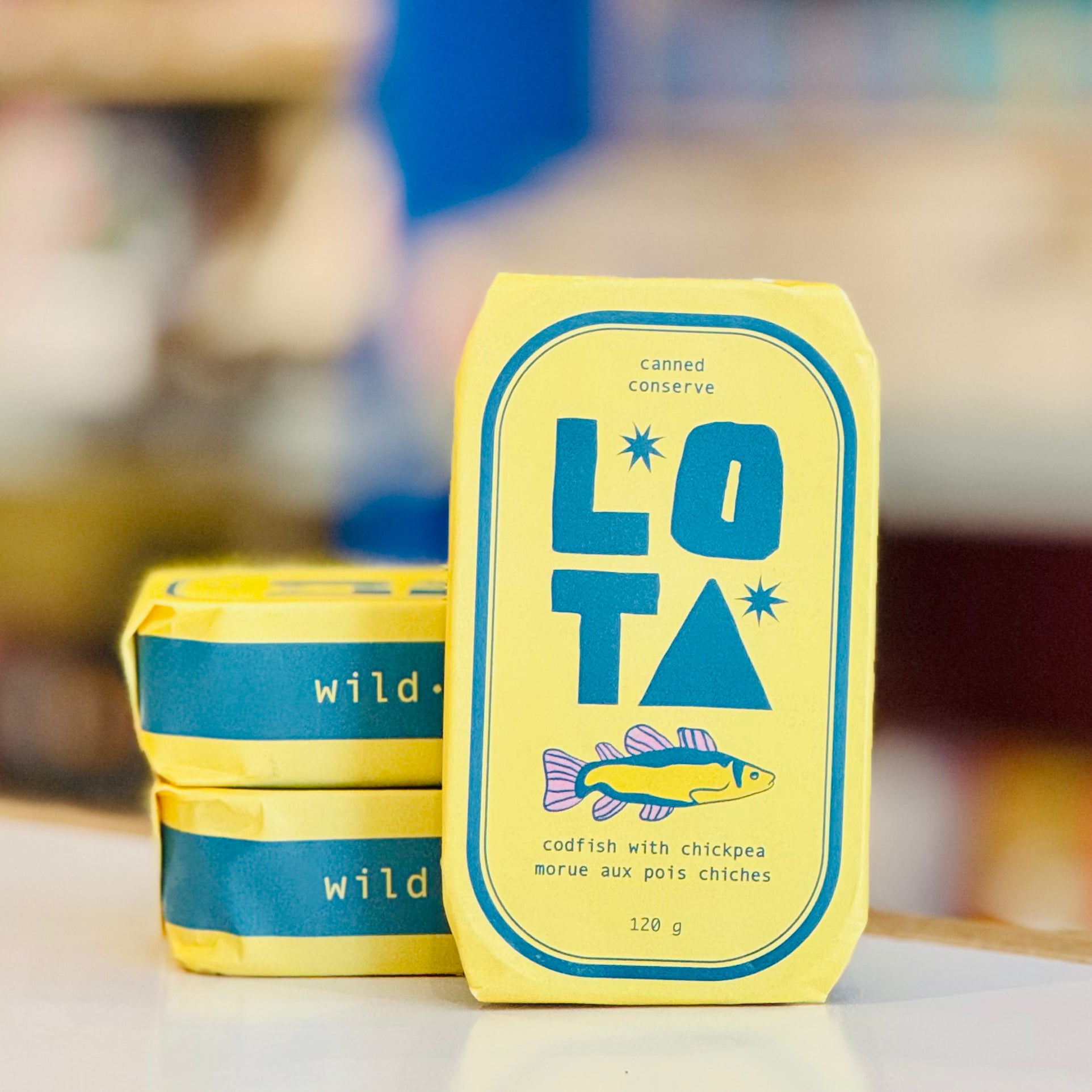 Yellow and blue LOTA canned conserve packaging on a blurred background