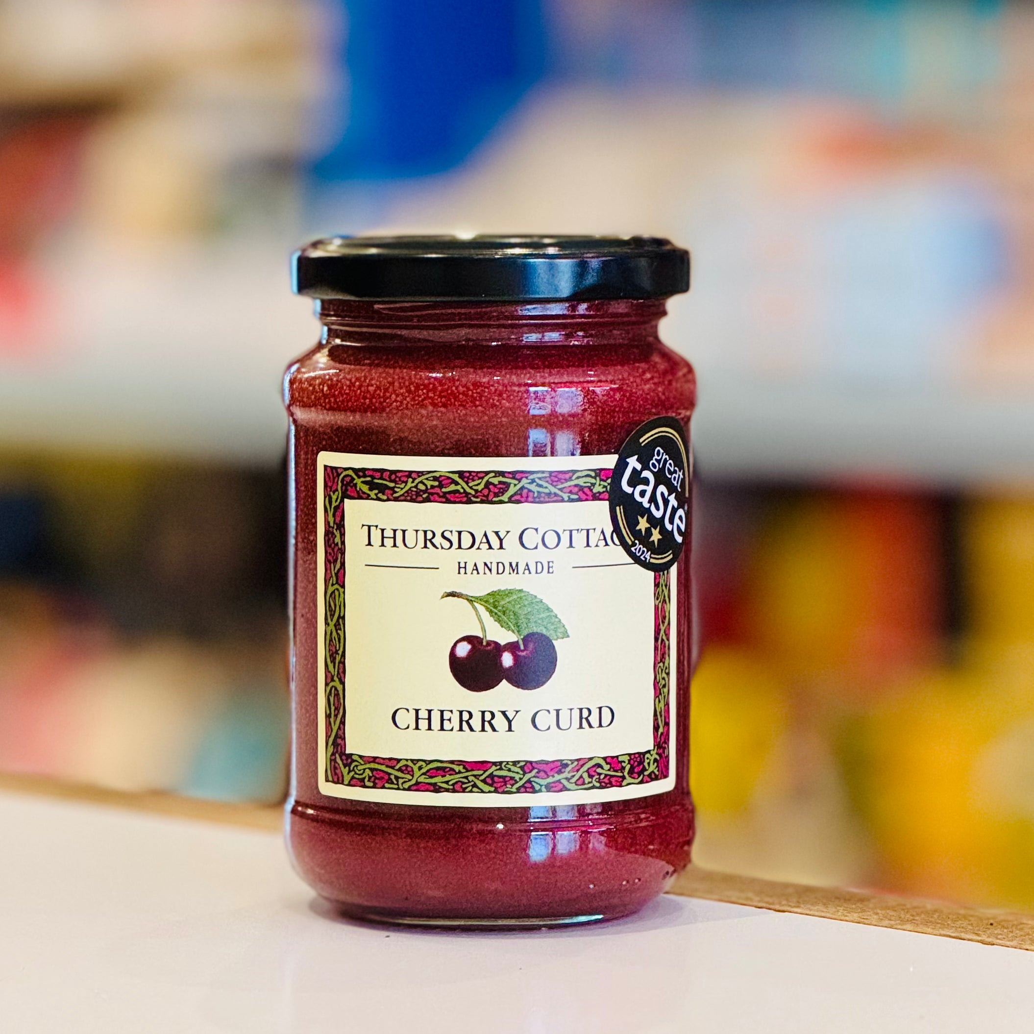 Jar of Thursday Cottage Cherry Curd with a label on a blurred background