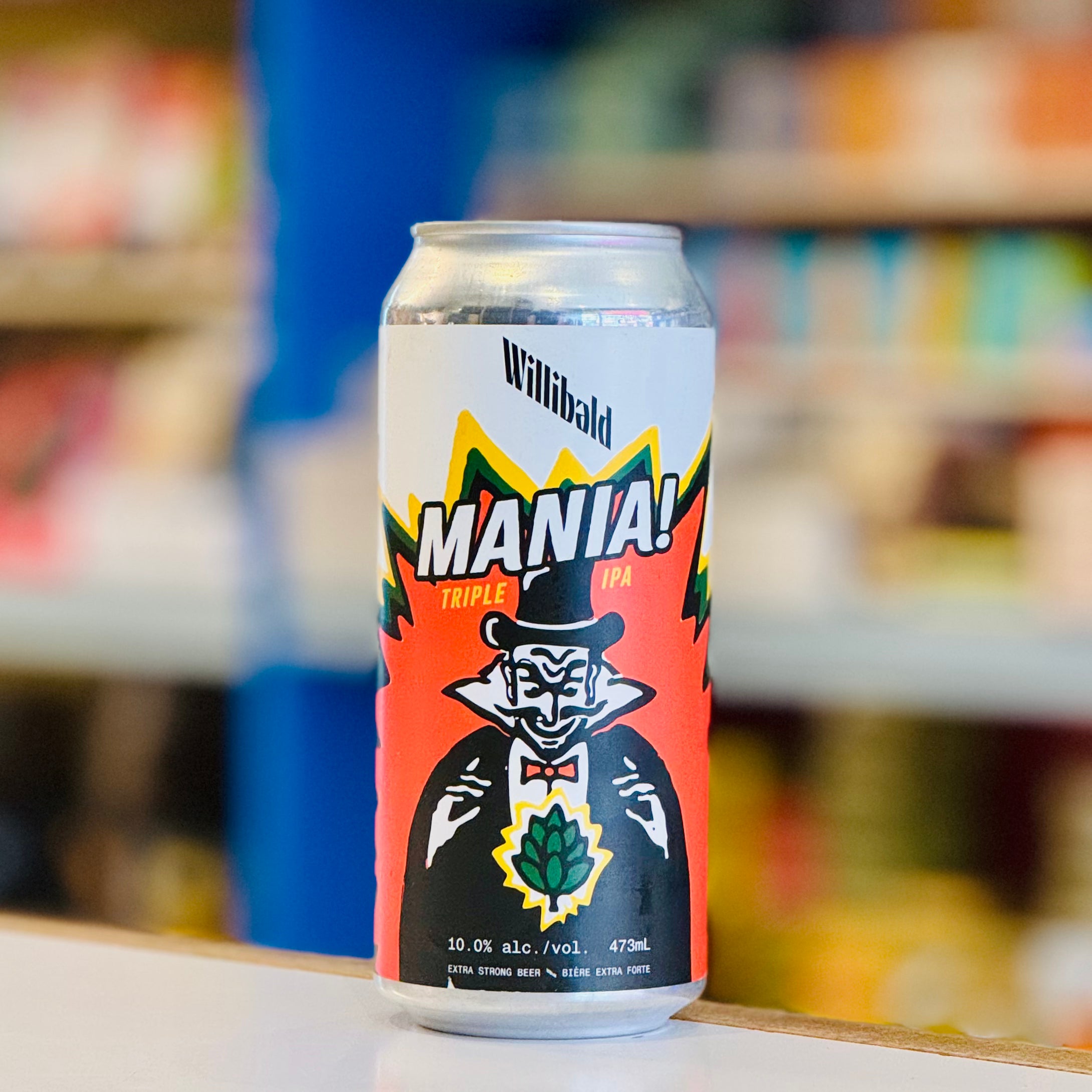 Beer can with 'Mania!' branding on a blurred store shelf background