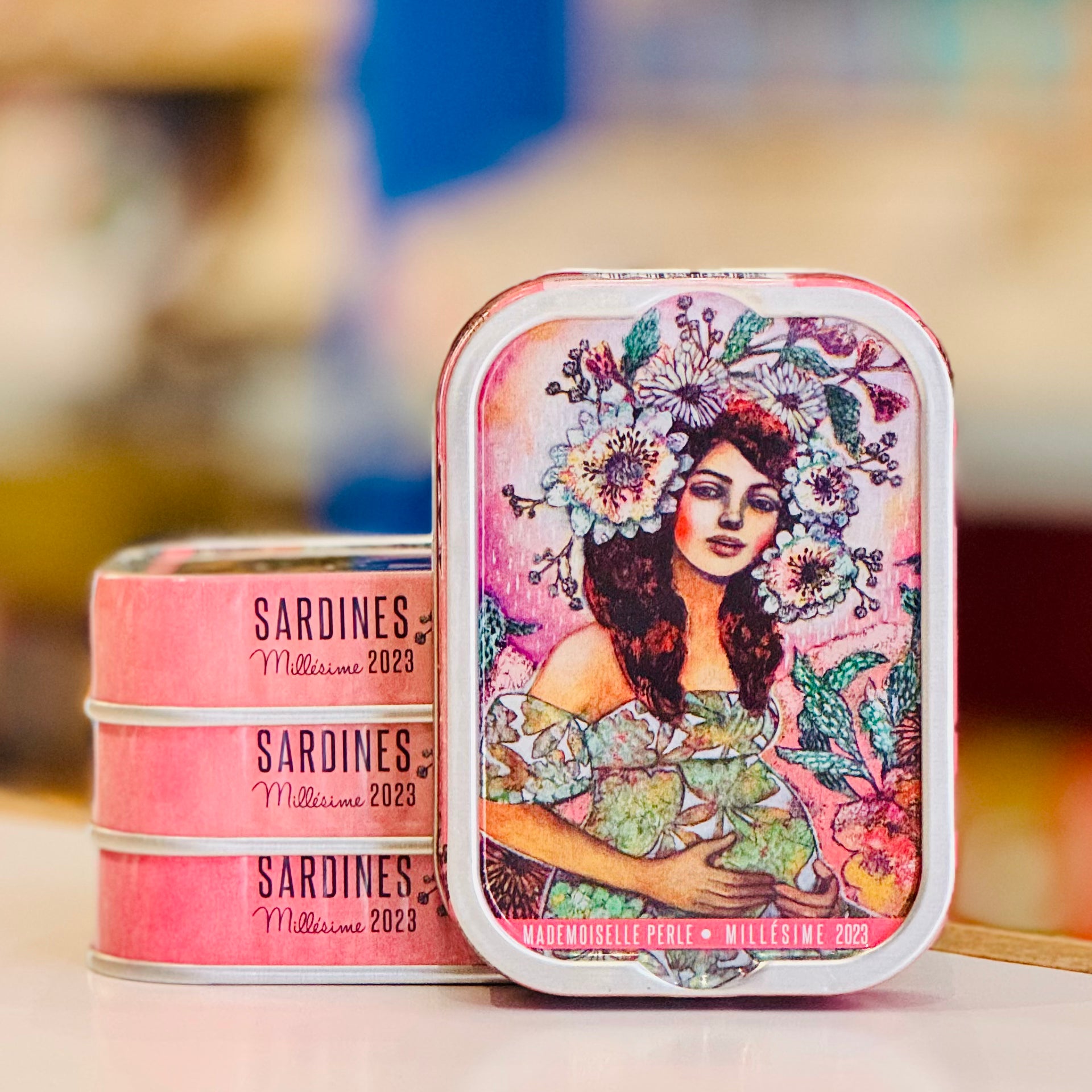 Decorative tins with artistic designs and 'Sardines Millésime 2023' text on a blurred background