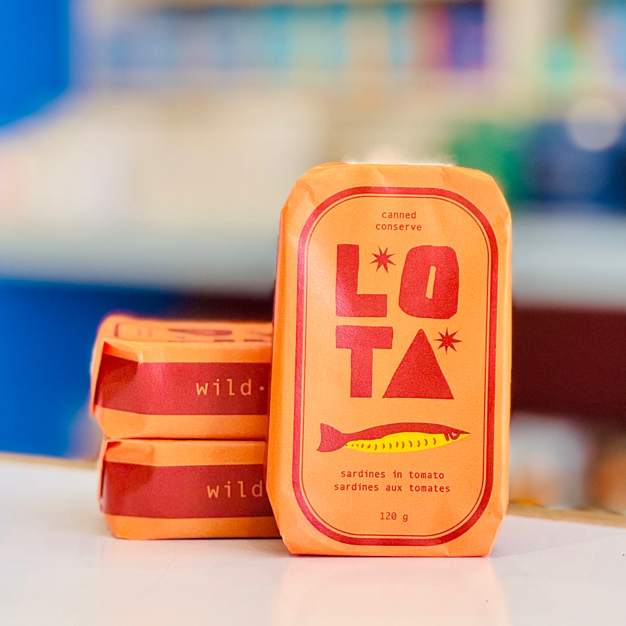 Two LOTA canned sardine packages on a white surface with a blurred background