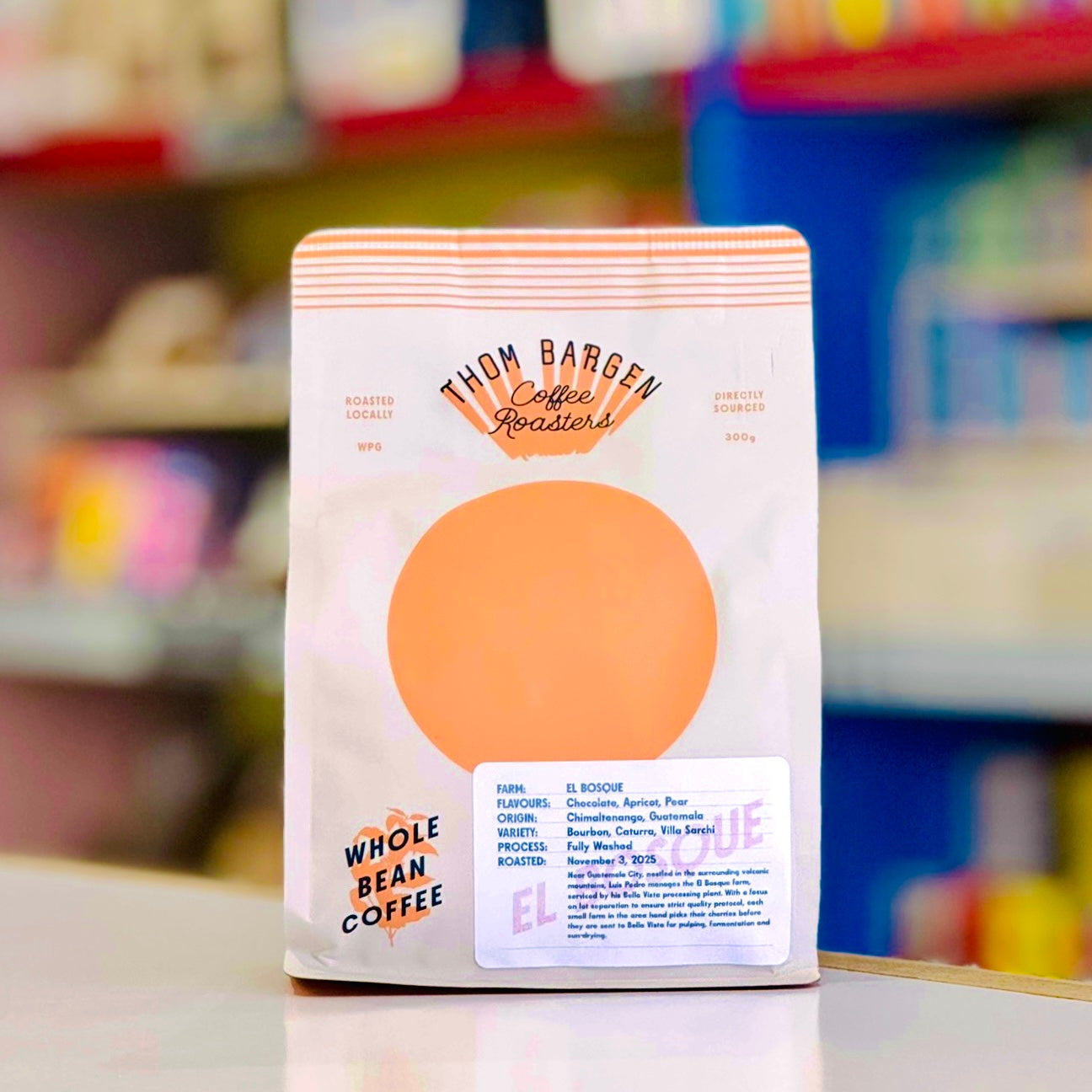 Coffee bag with 'Thom Barren Coffee Roasters' branding on a blurred store shelf background