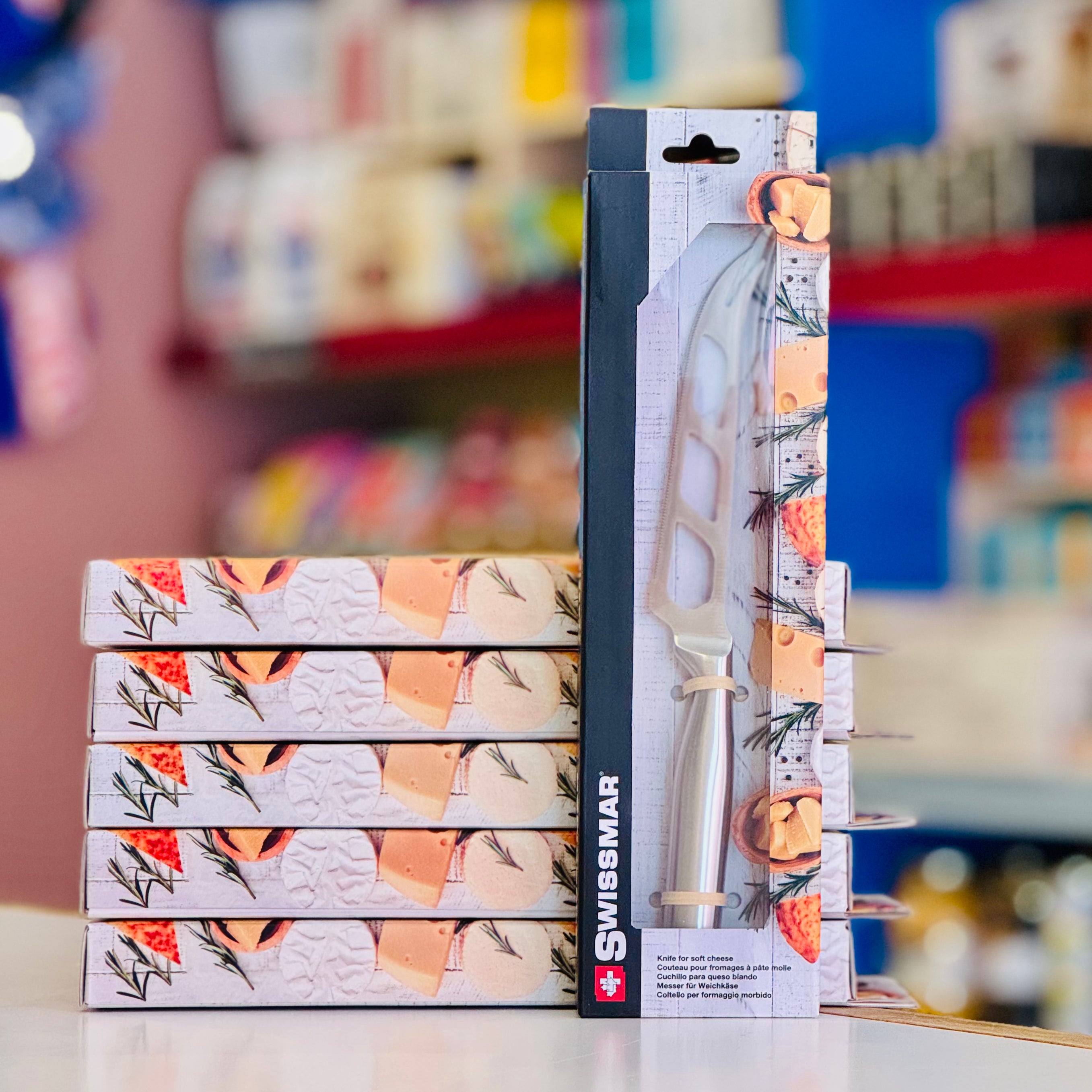 Stack of Swissmar pizza stone packaging with a blurred store shelf in the background