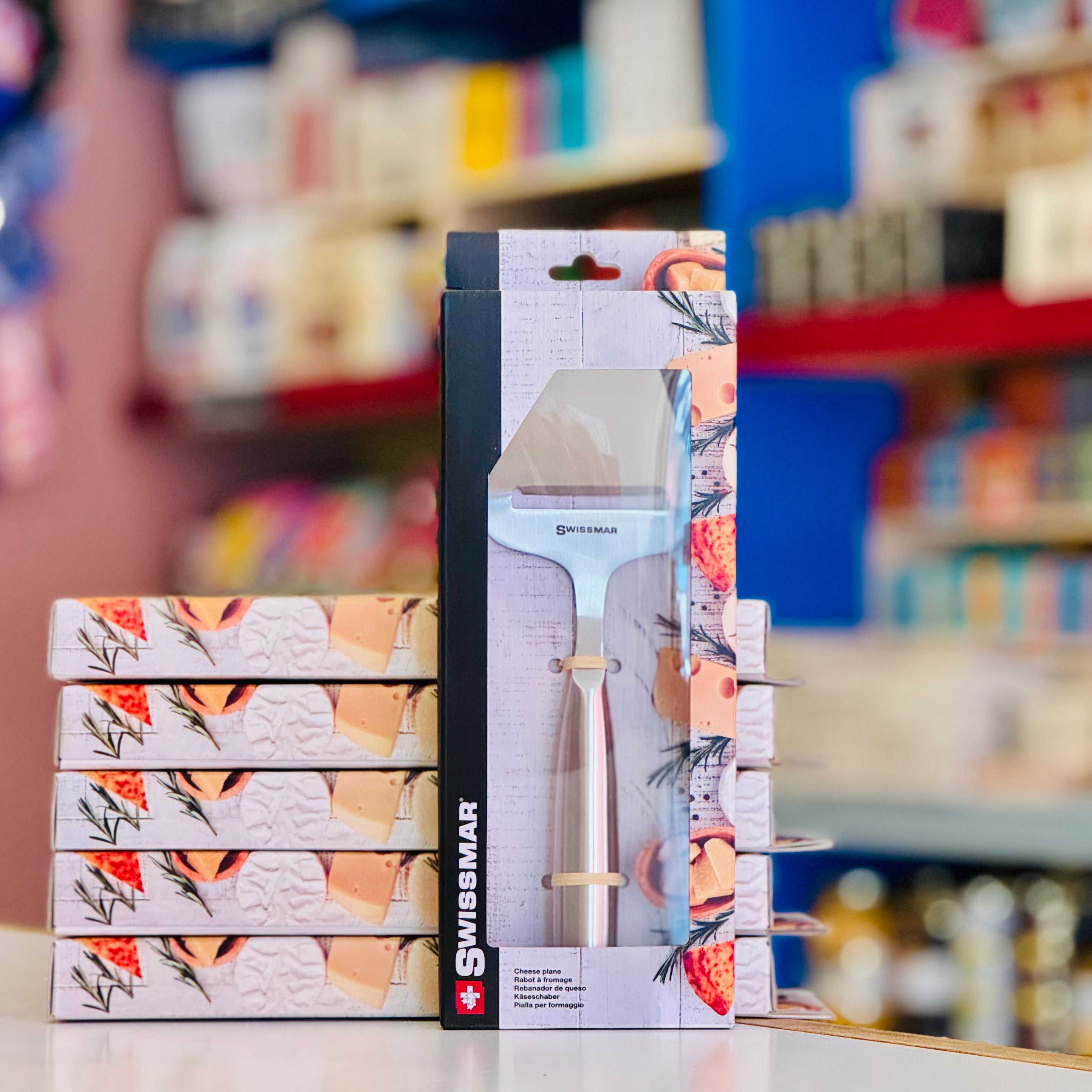 Stack of Swissmar branded kitchen shears packaging with a blurred store shelf in the background