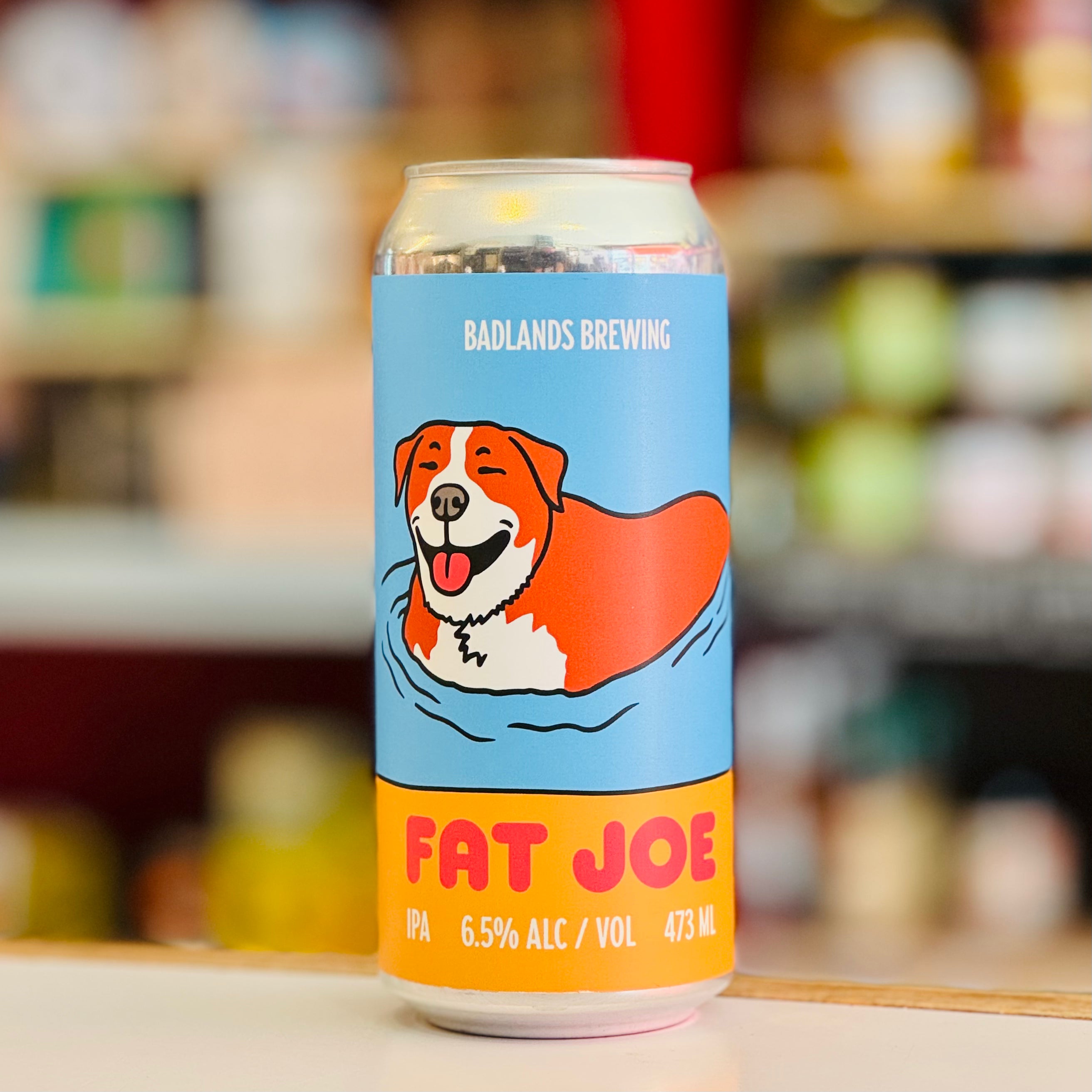 Beer can with a dog illustration and 'Badlands Brewing Fat Joe' text on a blurred background