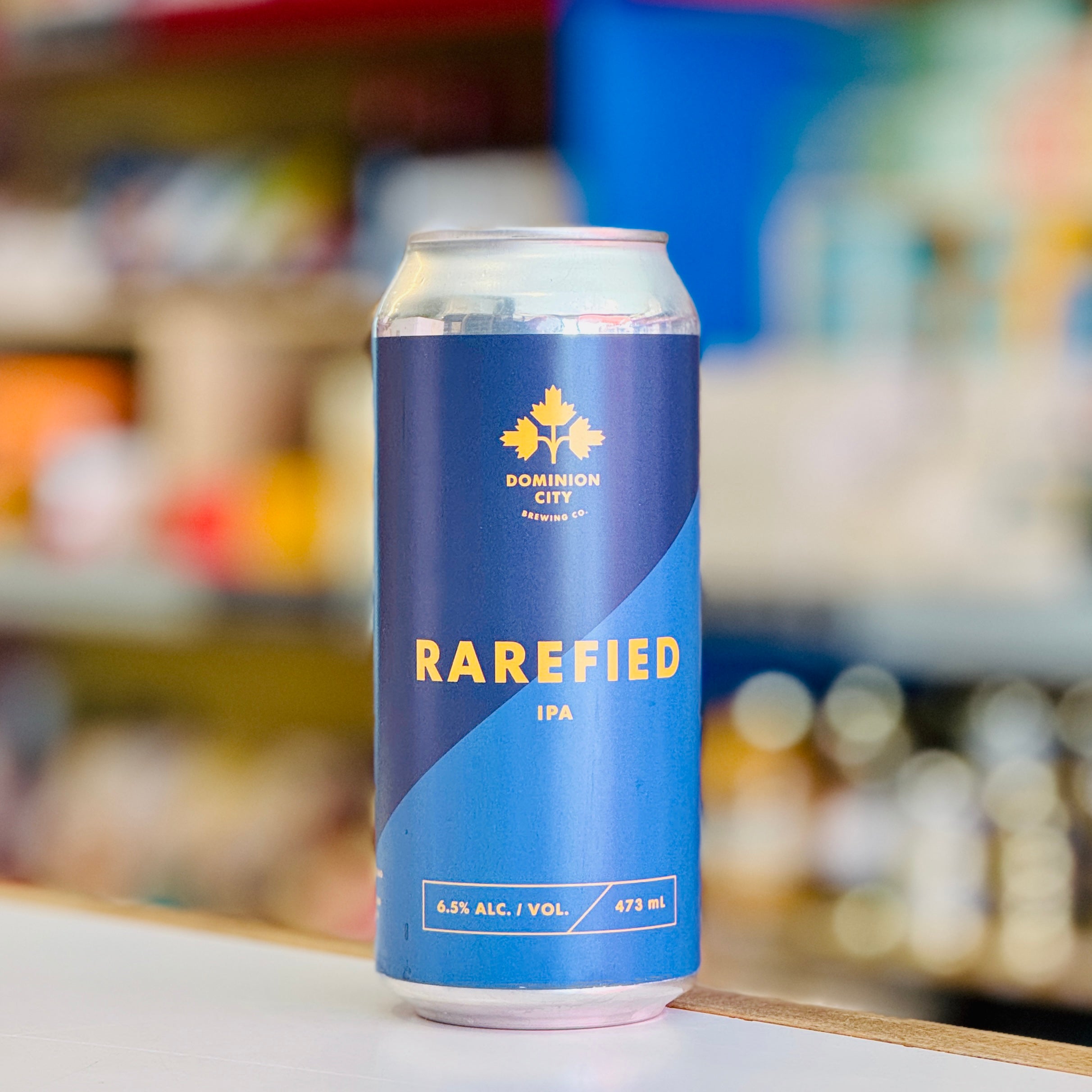 Blue can of Rarefied IPA with 'Dominion City Brewing' logo on a blurred store shelf background