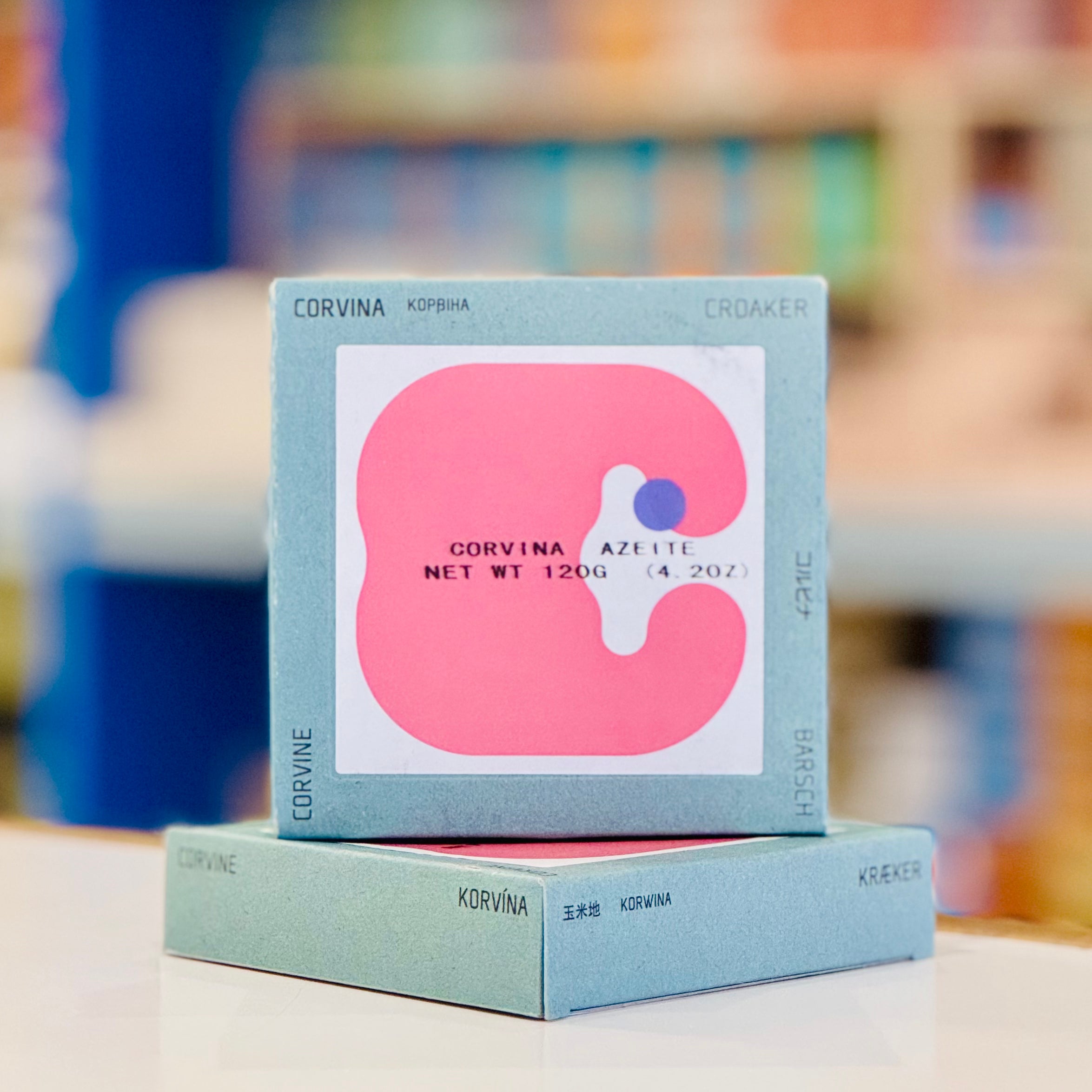 Two stacked boxes with a pink 'C' logo on a blurred bookshelf background