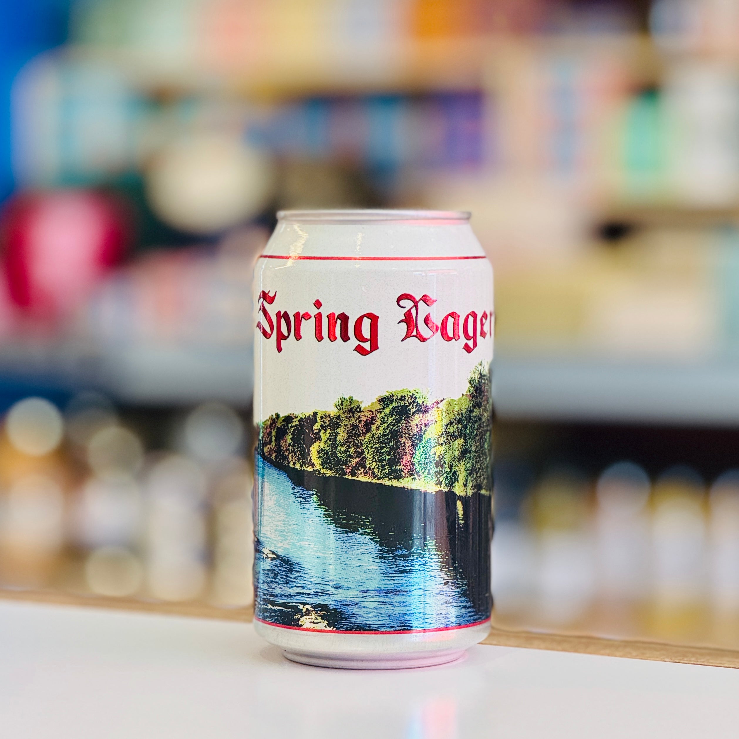 Can of 'Spring Lager' with a scenic design on a blurred bar background