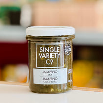 Jar of Single Variety Co. Jalapeno Jam on a wooden surface with a blurred background