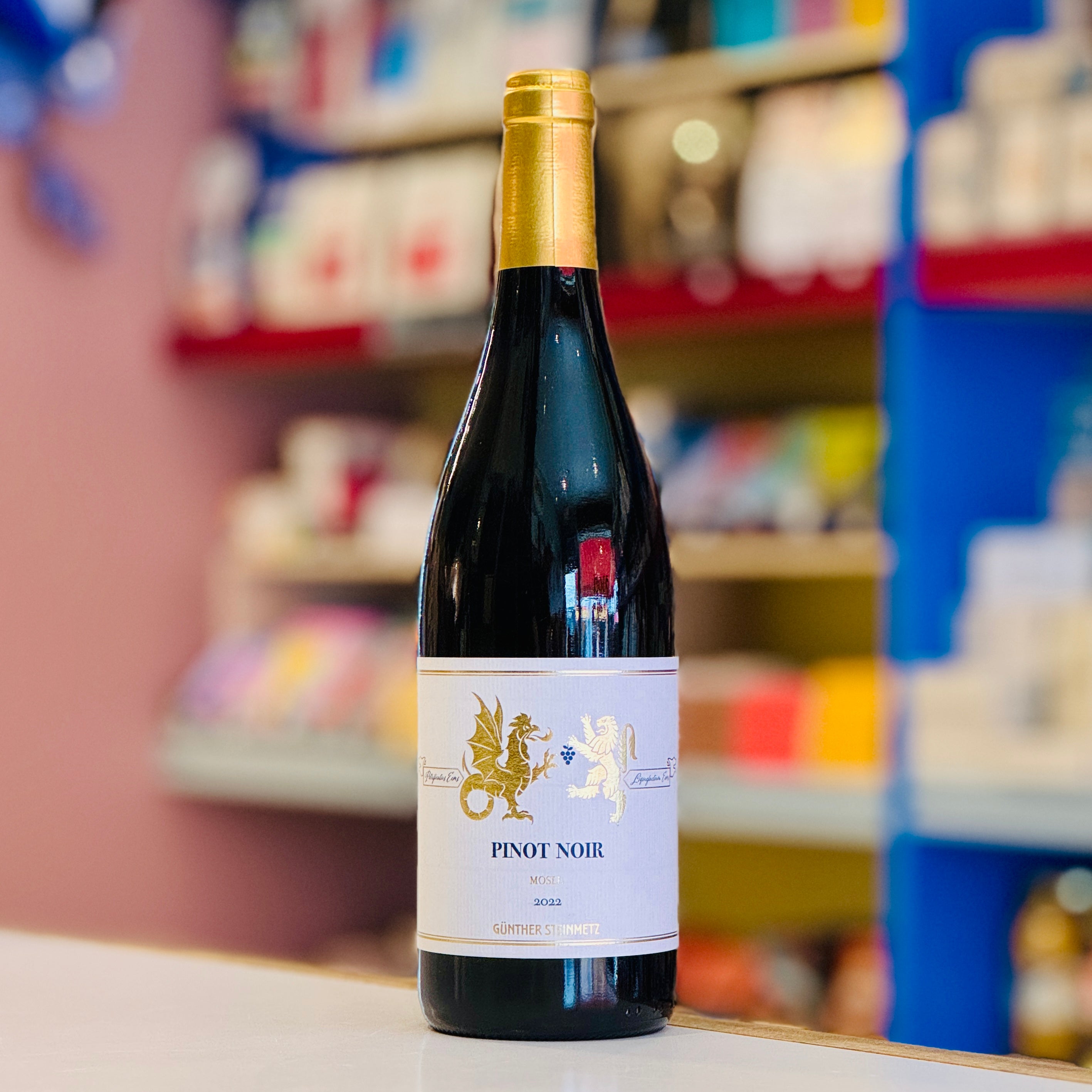 Bottle of Pinot Noir wine with a gold label on a shelf in a store.