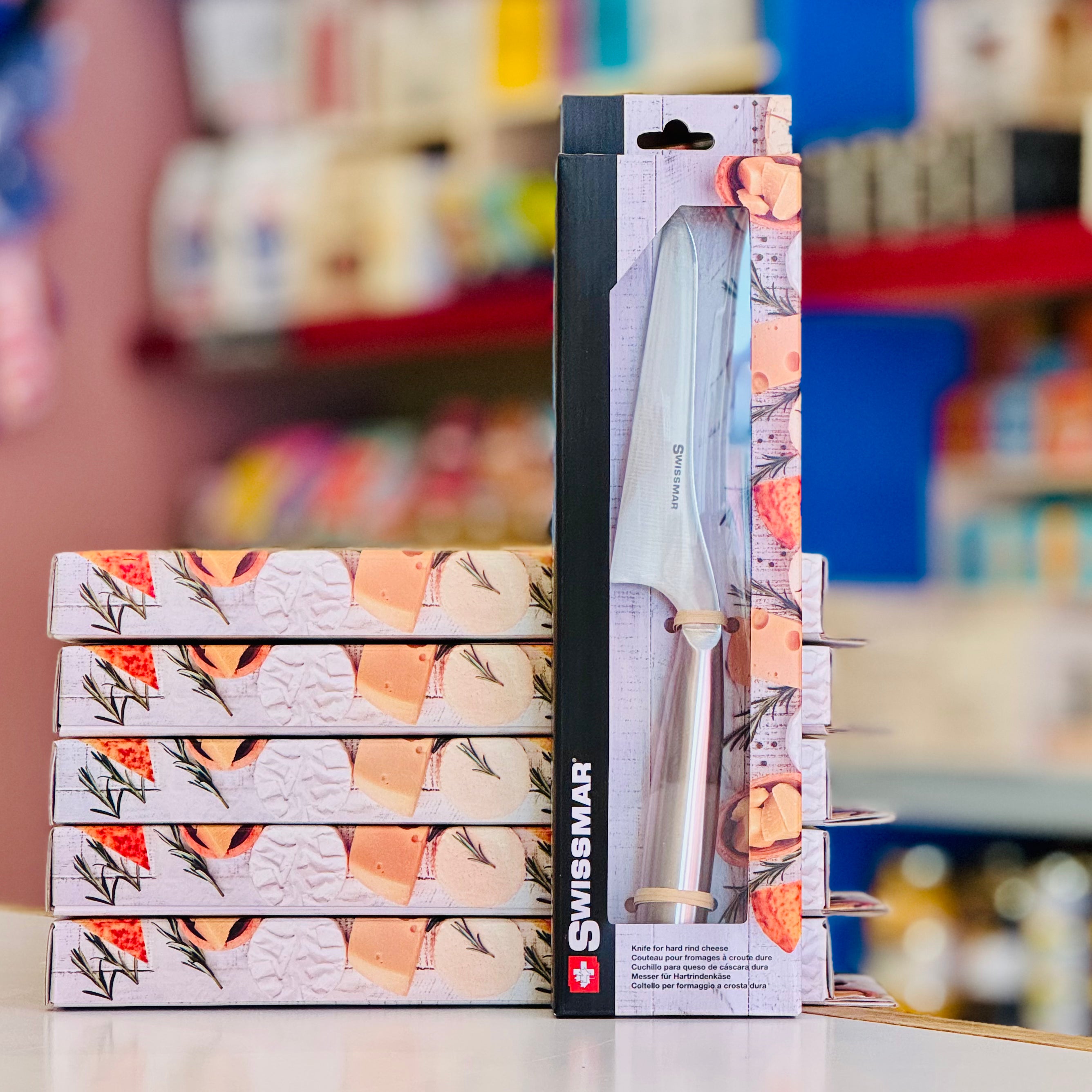 Stack of Swissmar knife boxes with a knife in packaging on a blurred store shelf background