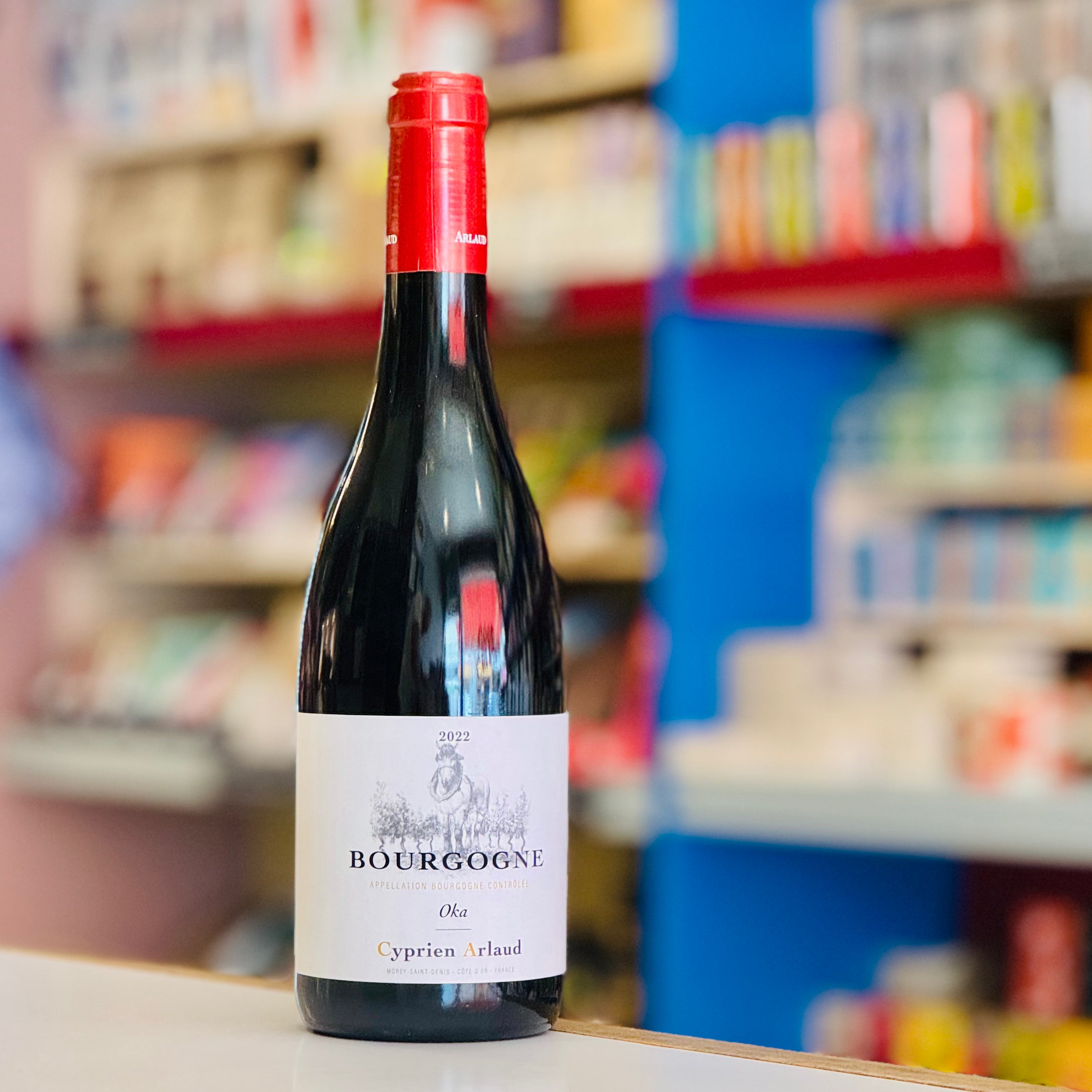 Bottle of Bourgogne wine with a red cap on a shelf in a store.